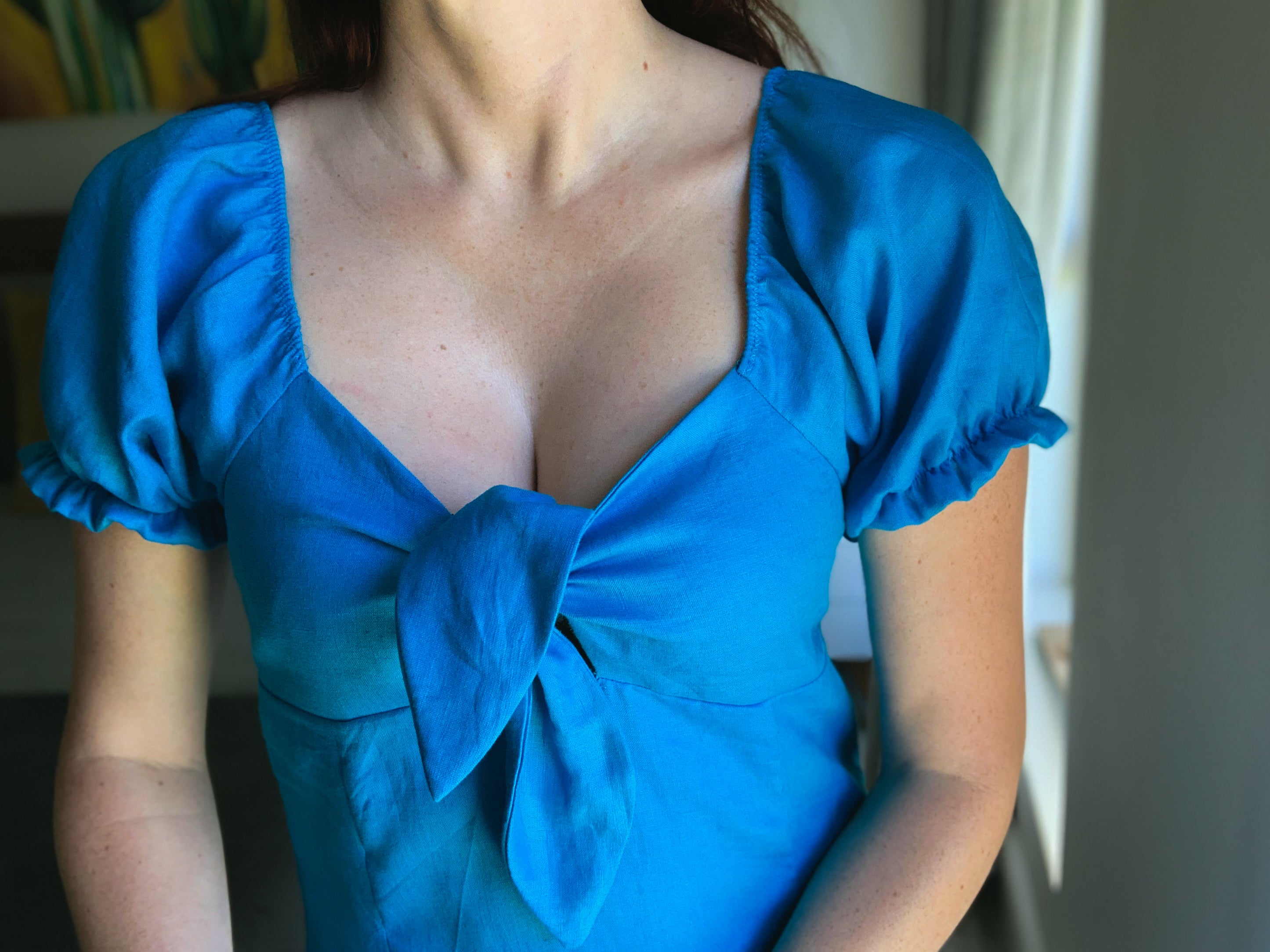 Close-up detail of puff sleeve dress and knot detail at bust of blue linen dress.