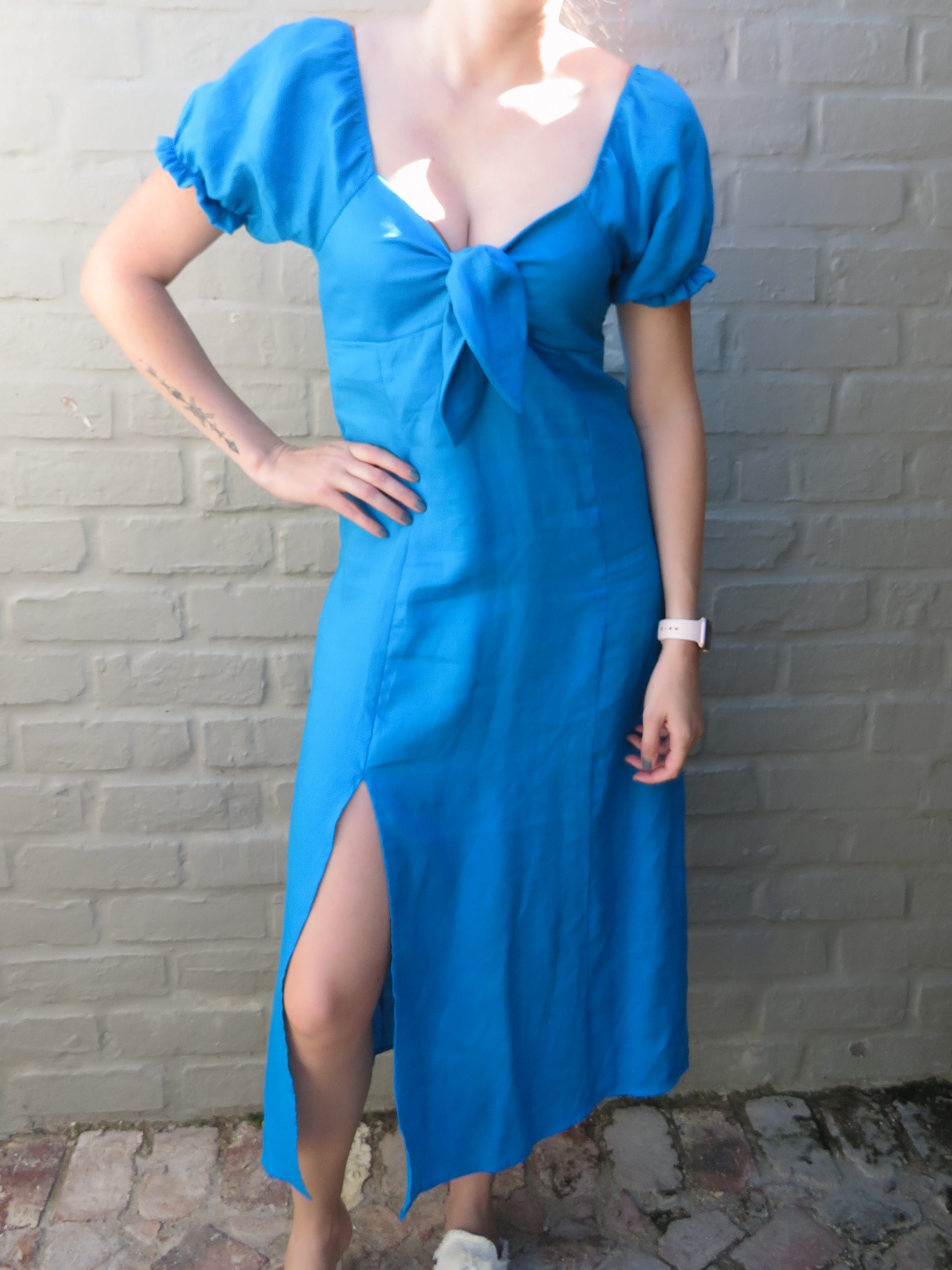 Person wearing a midi length turquoise blue dress with a bust tie detail and puff short sleeves and knee slit.
