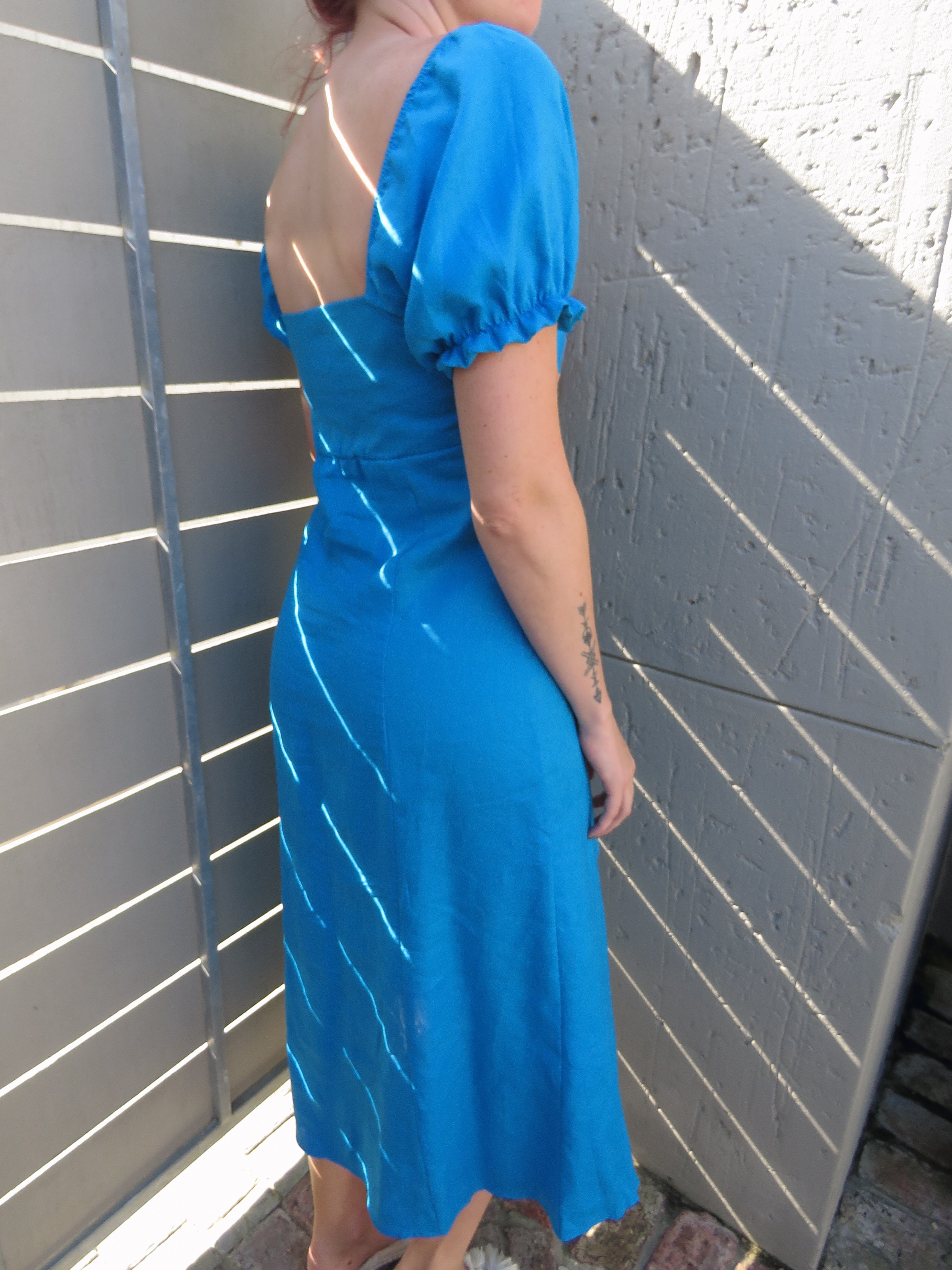Back side view of puffed sleeve midi dress  with open upper back detail, made from turquoise blue pure linen.