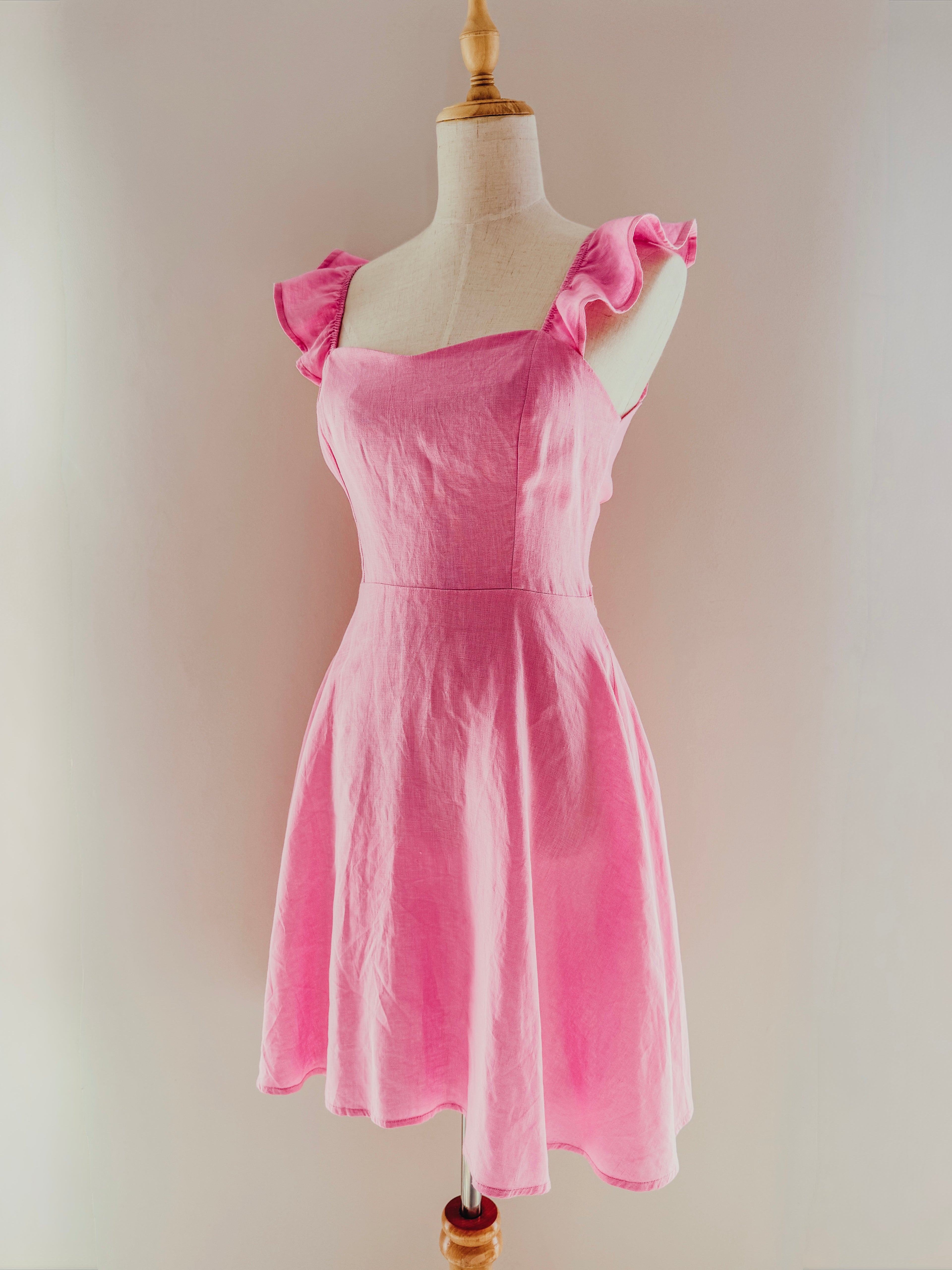 Candy pink mini dress with frilly straps and corset style upper body on a mannequin.