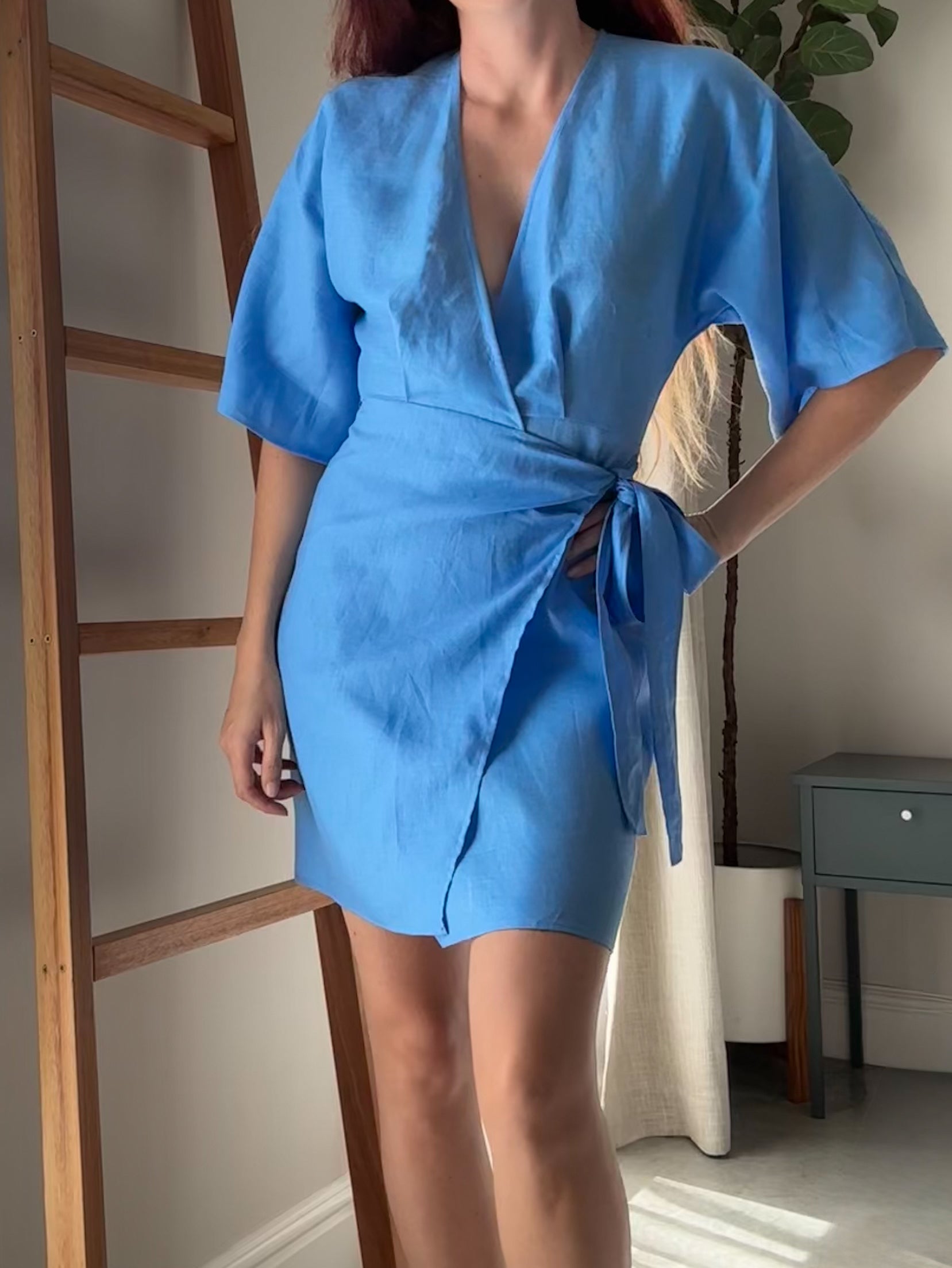 Woman wearing a short blue dress made from pure linen in a wrap style with kimono sleeves.
