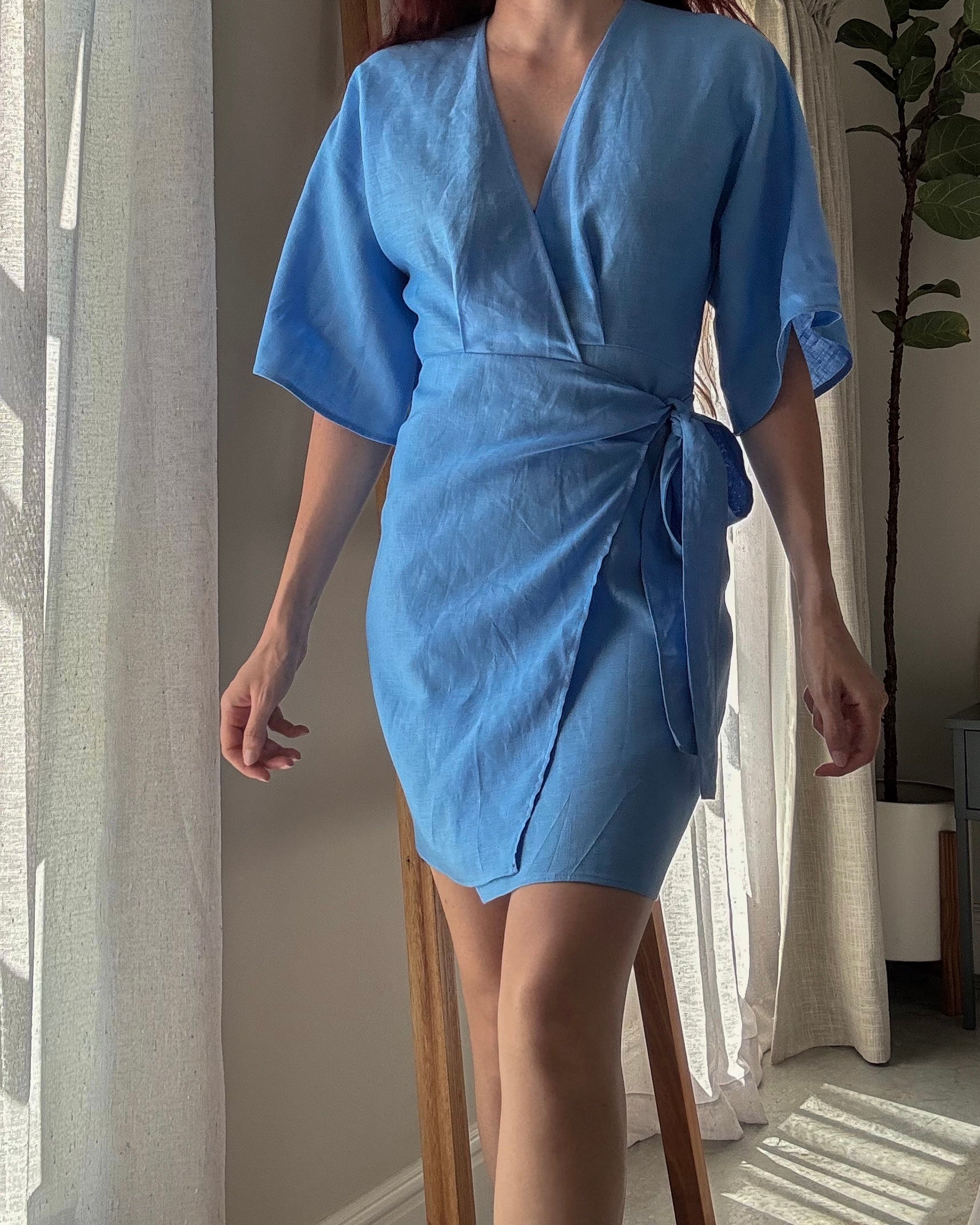Person wearing a light blue dress with kimono sleeves and wrapped in waist with side tie.