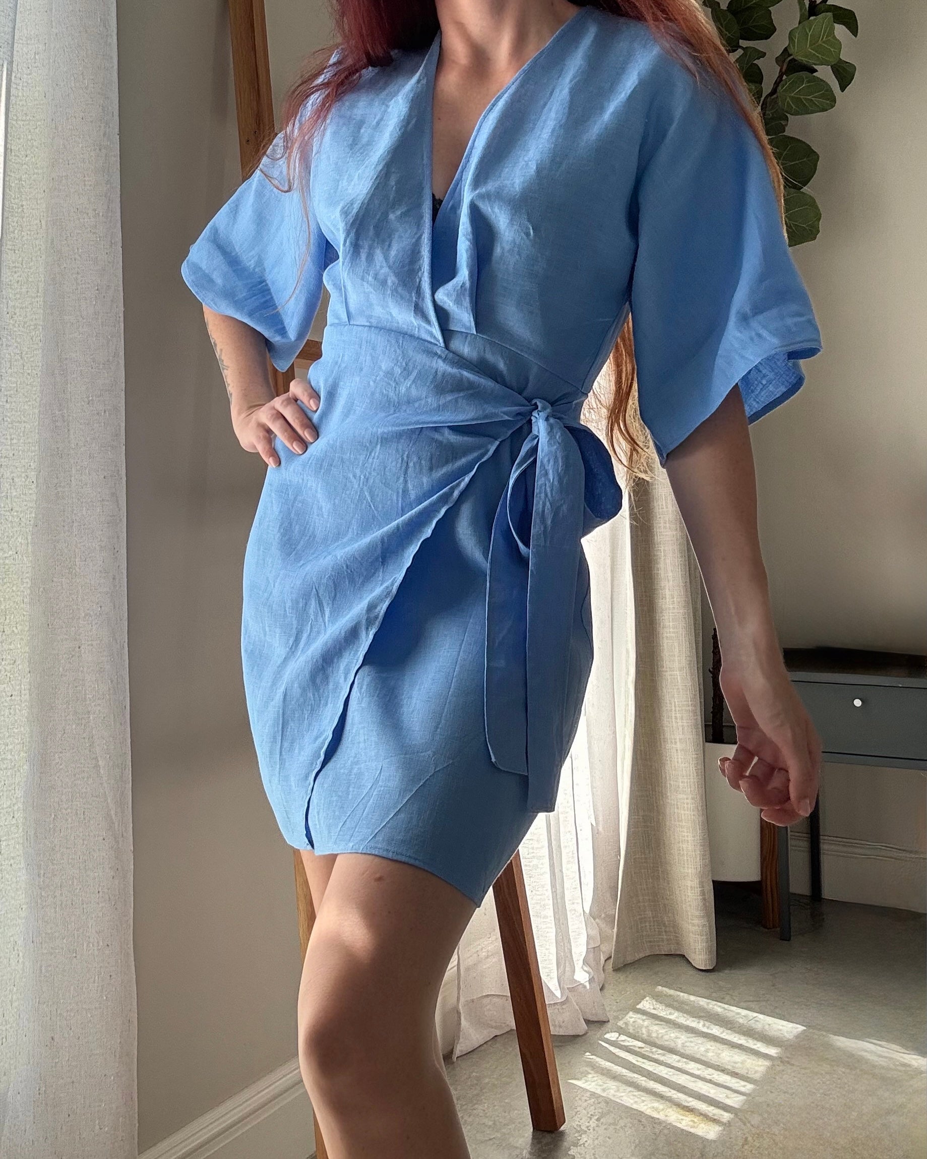 Person wearing a marina blue wrap dress made from pure linen with kimono sleeves.