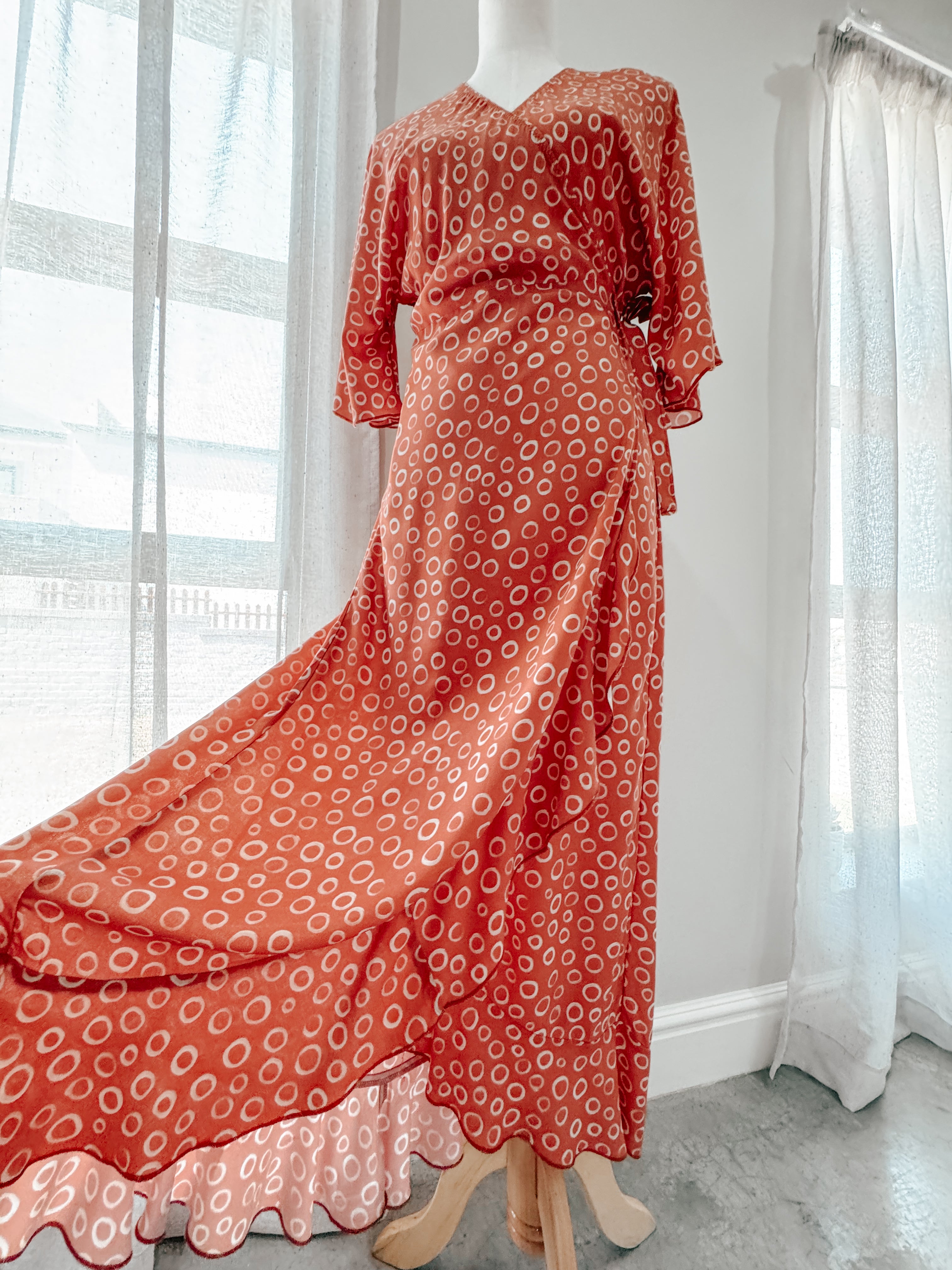 Rust colour with white circular print wrap dress with kimono sleeves on mannequin showcasing the volume at the bottom of the dress and movement of the frilled hem.