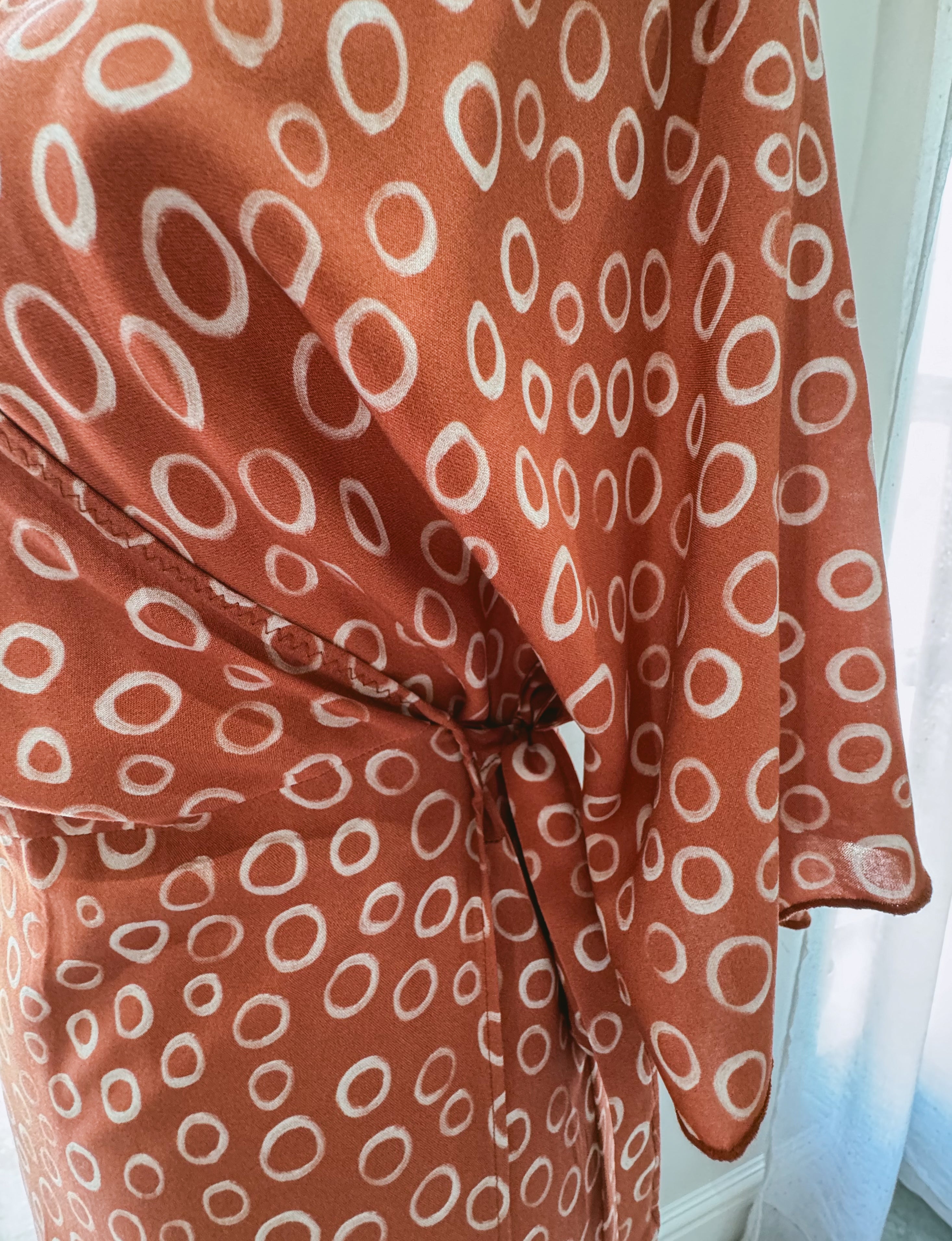 Close up of side tie on wrap dress made from rusty brown Ecovero Viscose fabric with white circular pattern.