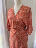 Close up of upper body of rust colour with circular print wrap dress with kimono sleeves.