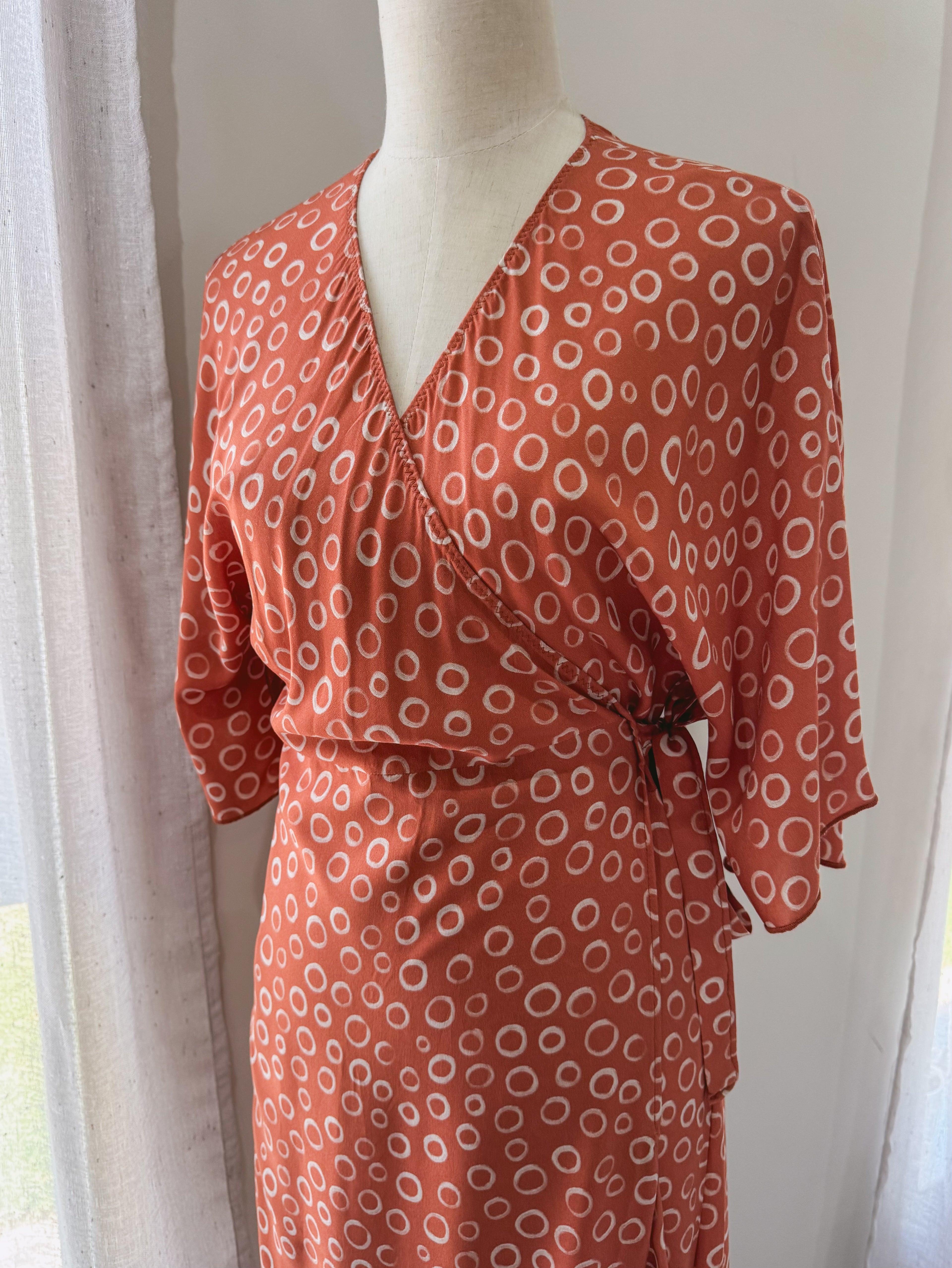 Close up of upper body of rust colour with circular print wrap dress with kimono sleeves.