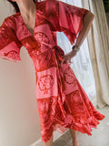 Person wearing a red & pink fruit and shells patterned wrap dress made from ecovero viscose, featuring movement in kimono sleeves and frilled hem of bottom.