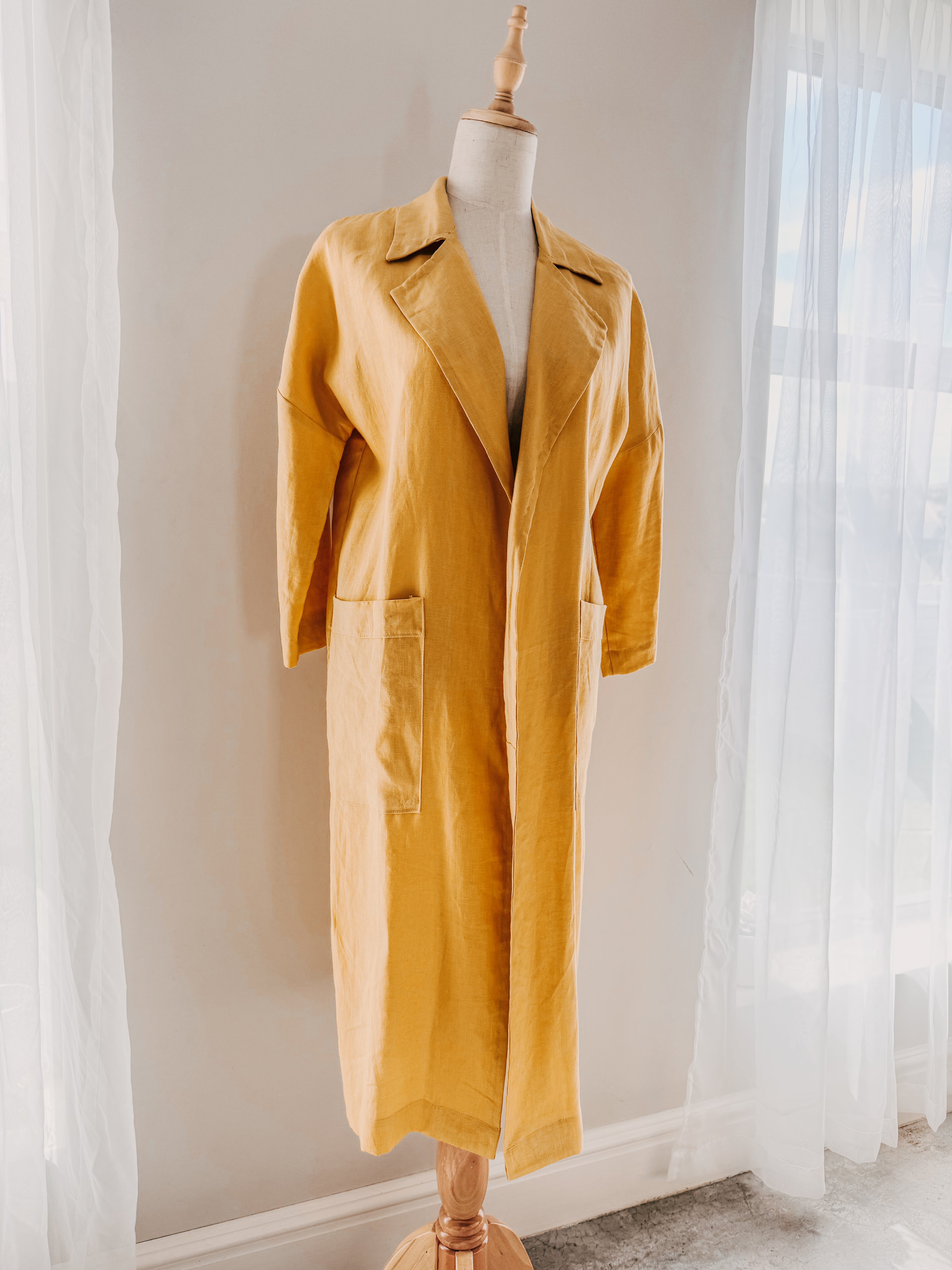 Yellow pure linen coat in relaxed fit with large front patch pockets and open lapel on a mannequin.