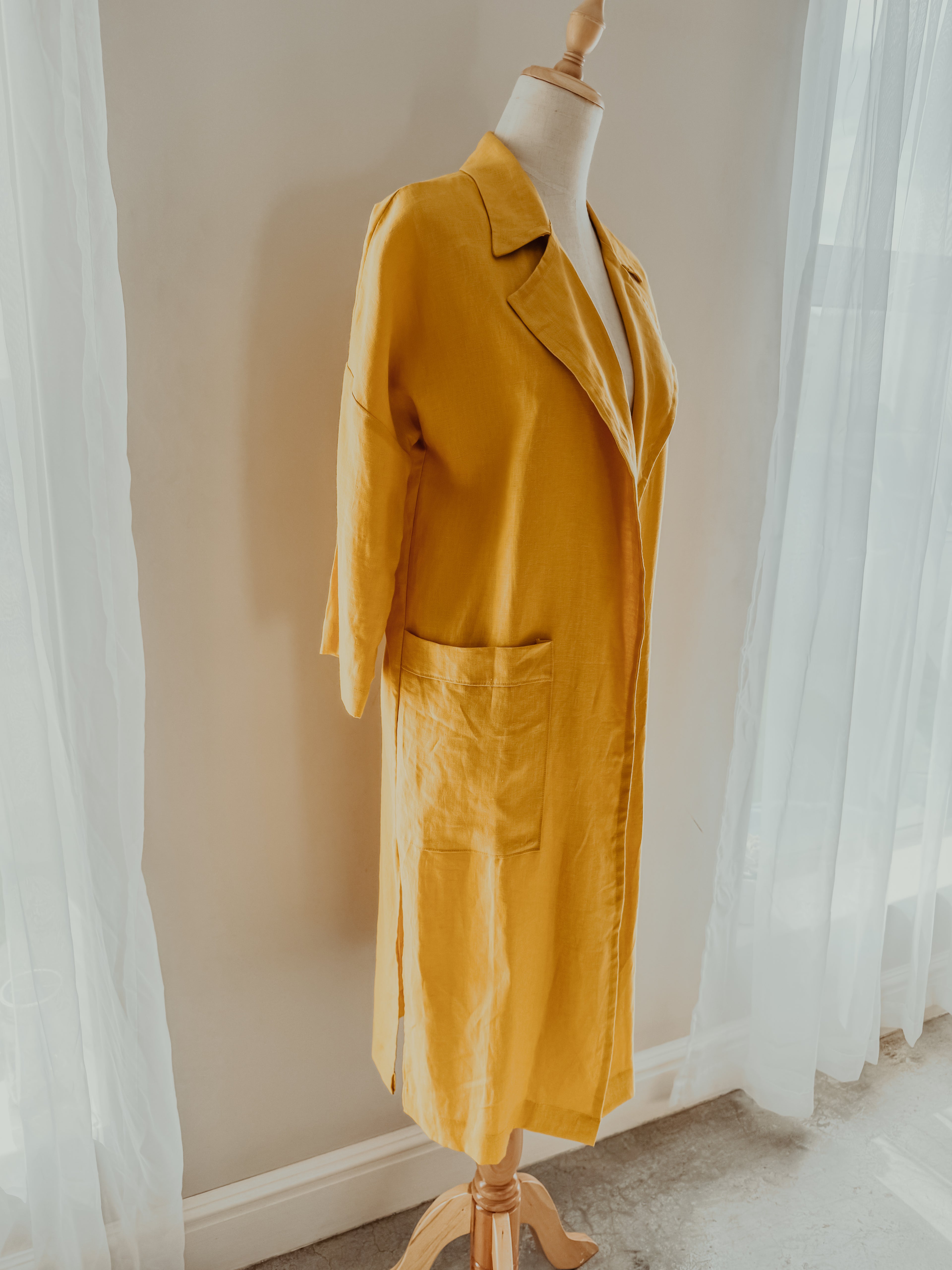 Side view of yellow pure linen coat on a mannequin in relaxed fit with large front patch pockets, open lapel and side slits.