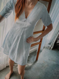 Person wearing a light blue pure linen dress with v-neckline and above knee length and above elbow sleeve length.