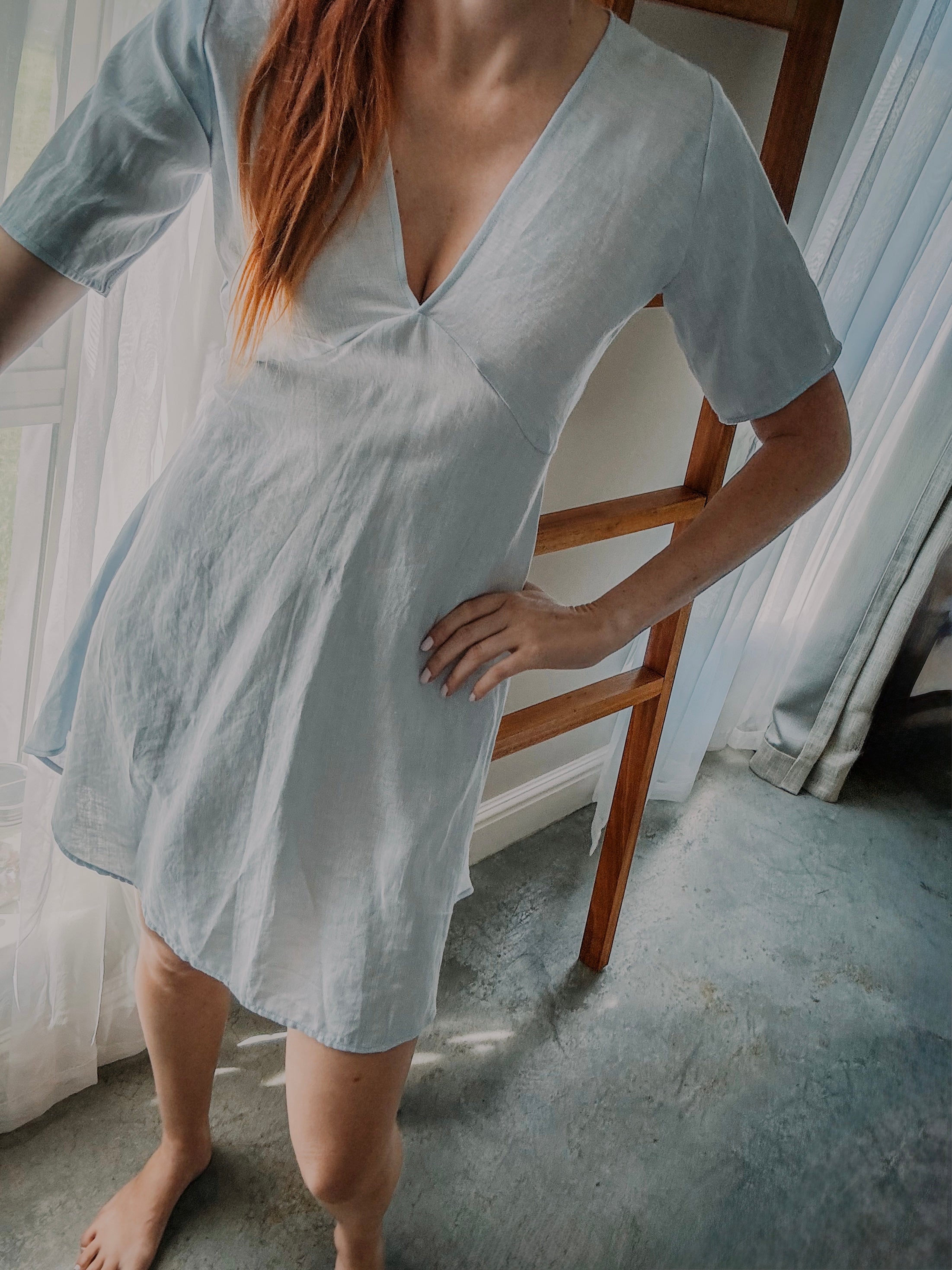 Person wearing a light blue pure linen dress with v-neckline and above knee length and above elbow sleeve length.