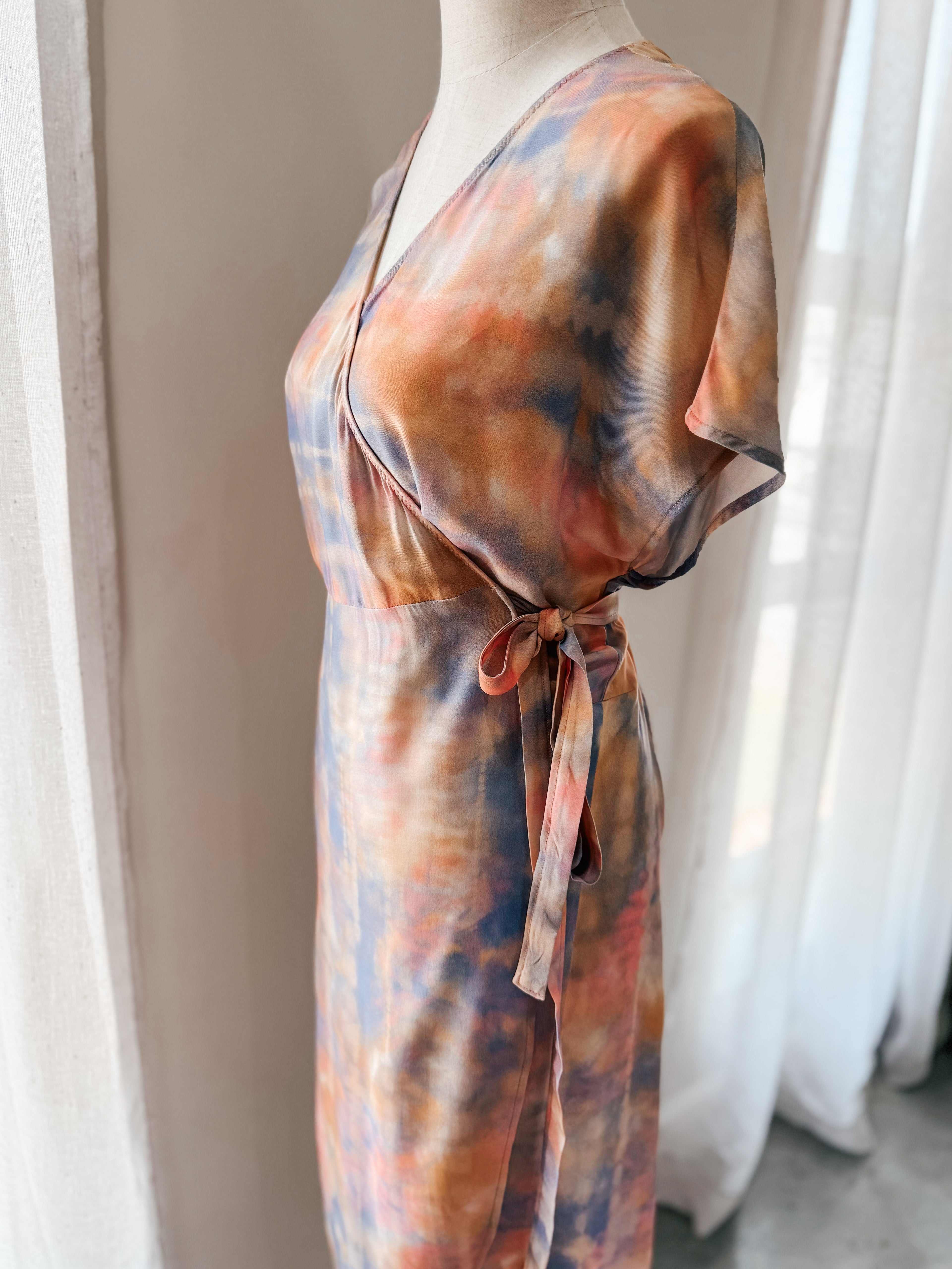 Close-up side tie view of tie-dye style print wrap dress in soft watercolour hues with relaxed grown on cap sleeve.