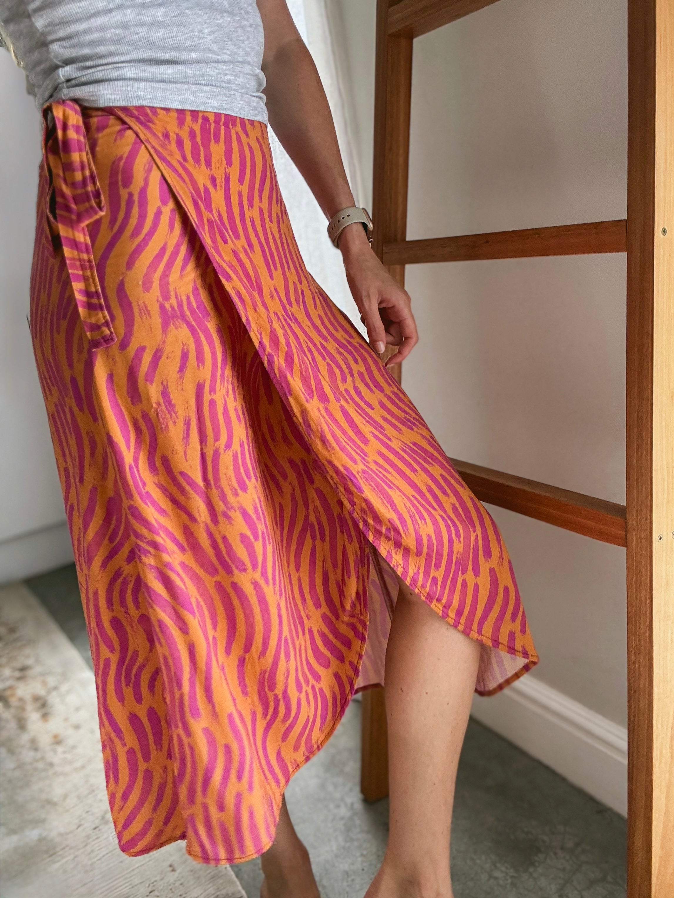 Person wearing a vibrant orange and pink brush stroke patterned midi wrap skirt made from Ecovero viscose.