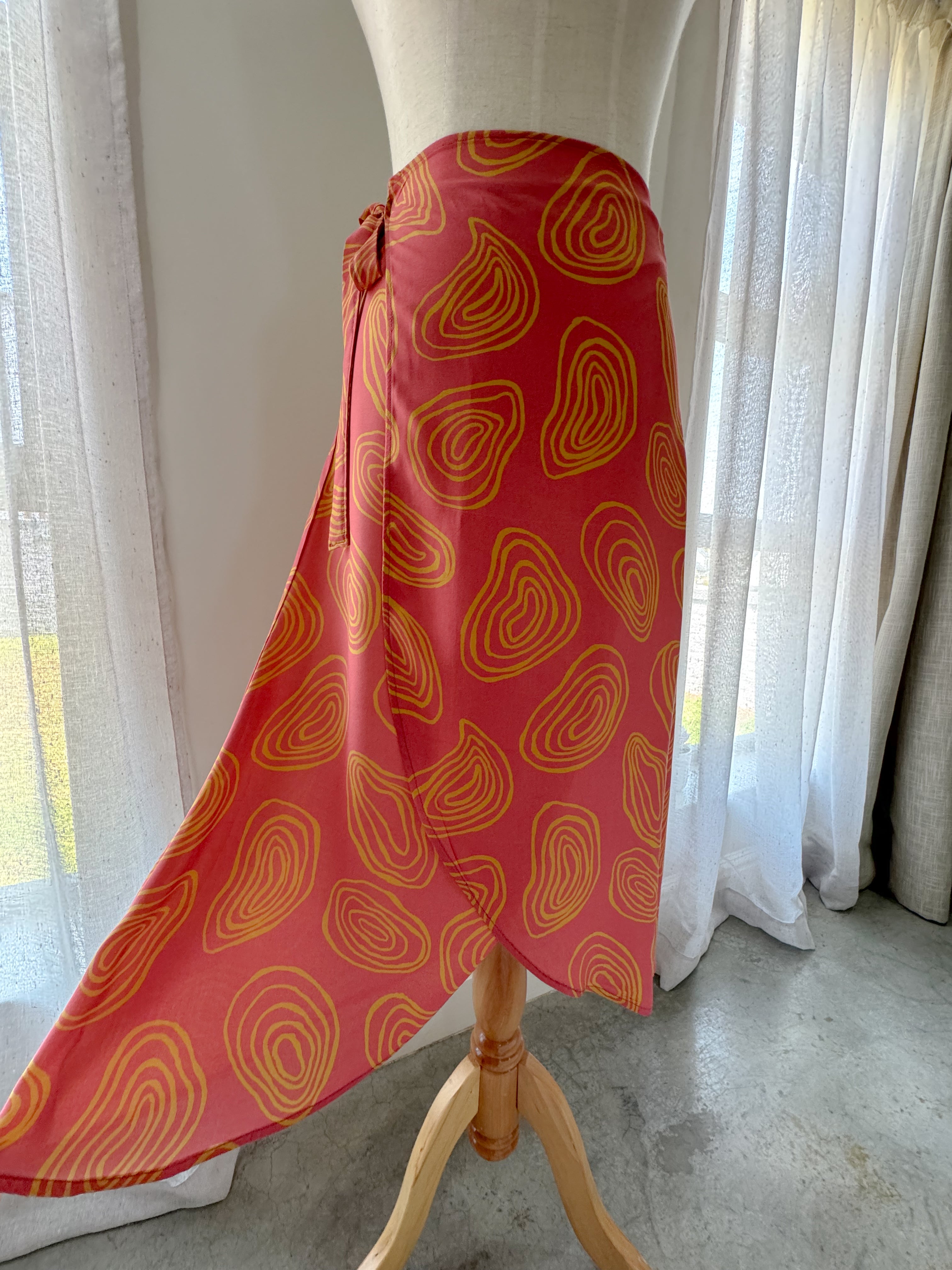 Coral colour high-waisted midi wrap skirt with yellow squiggle patterns made from Ecovero viscose and displayed on a mannequin to showcase the flare and movement provided in curved hemline.