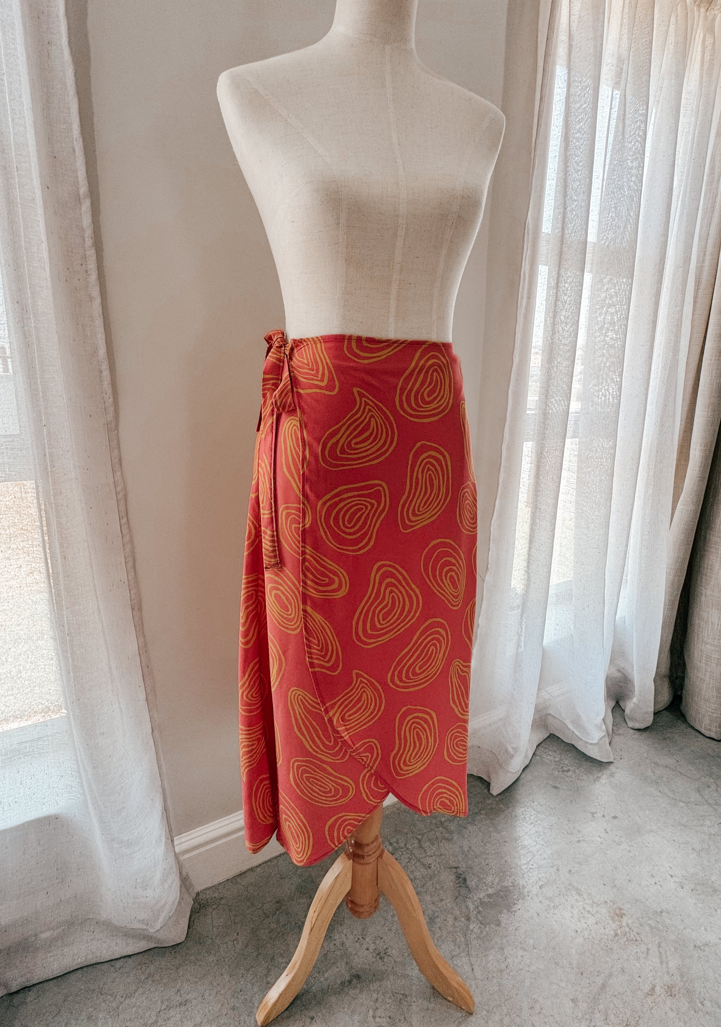 Coral colour high-waisted midi wrap skirt with yellow squiggle patterns made from Ecovero viscose and displayed on a mannequin to showcase the front curved hem.