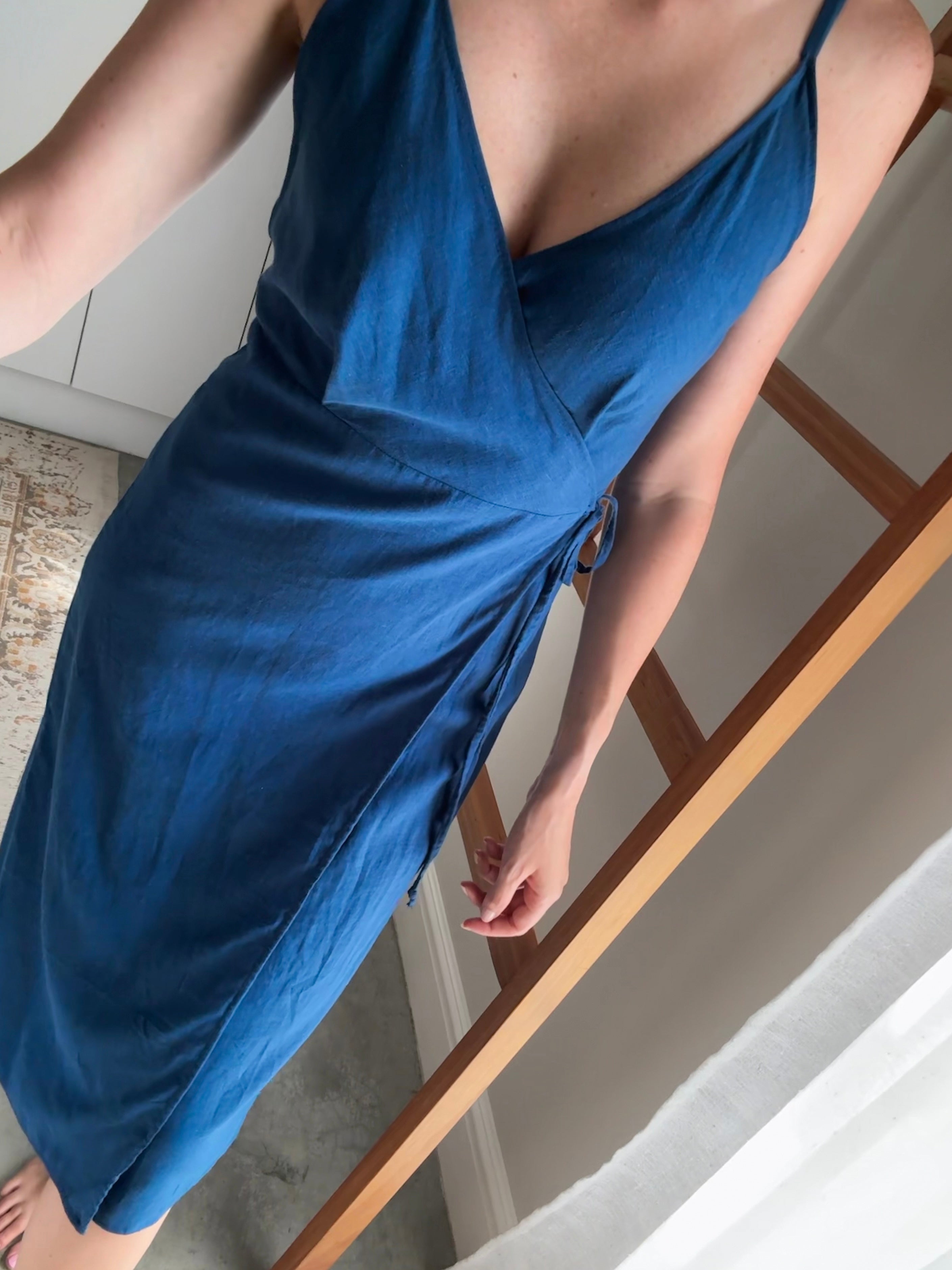 Person wearing a steel blue wrap dress with bust darts and midi length. 
