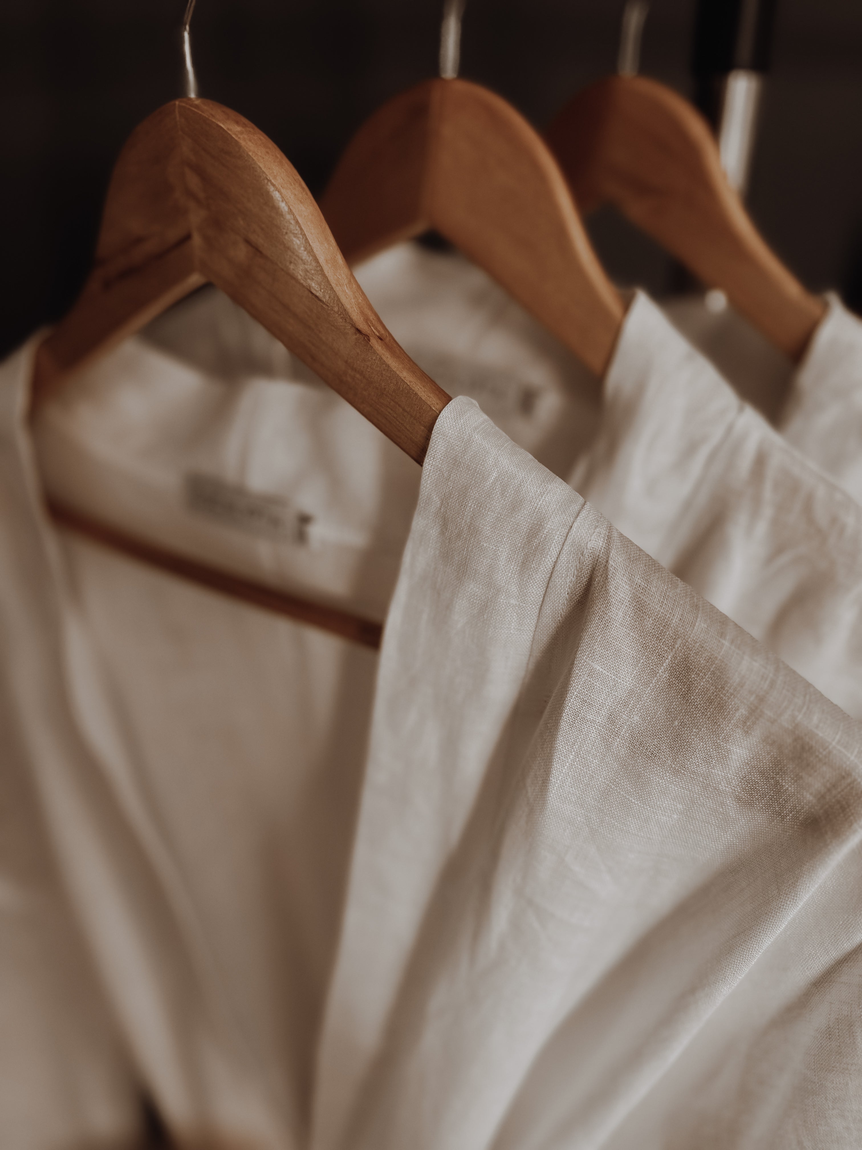 White bridesmaids linen gowns hanging on wooden hangers.