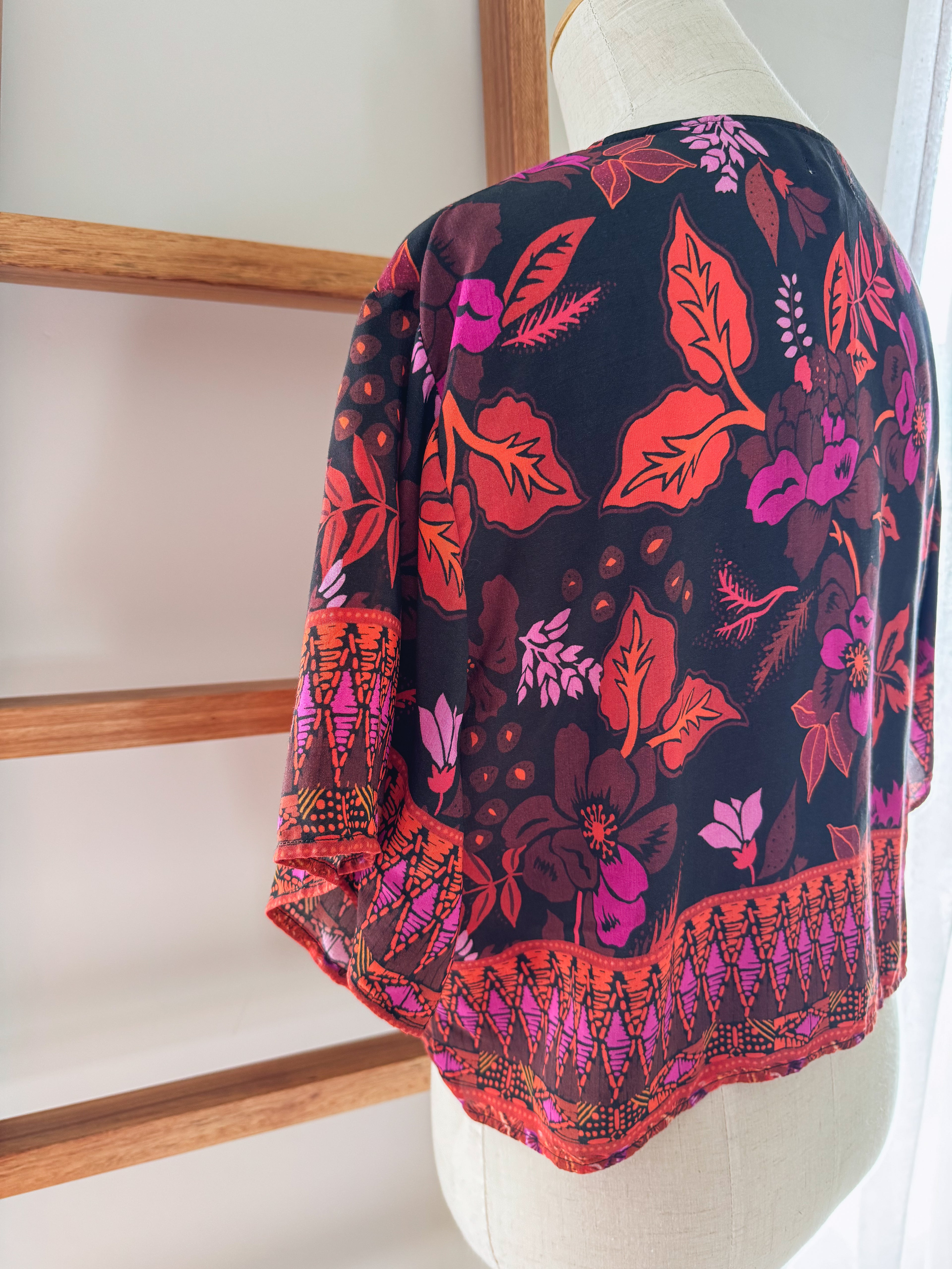 Colourful floral patterned top draped over a mannequin showing the back side view.