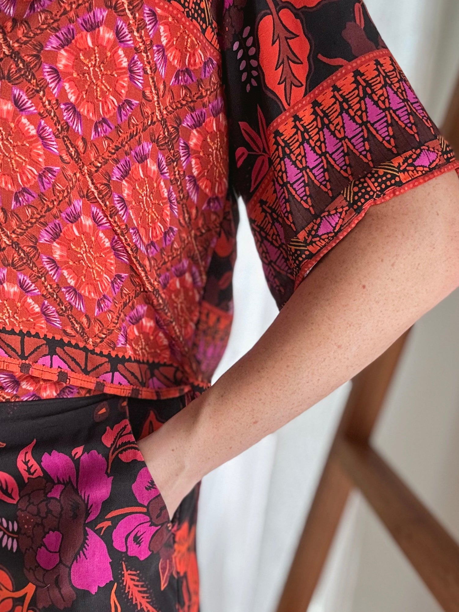 Close-up of a person wearing a colourful patterned outfit  with hand in pocket to showcase sleeve length.