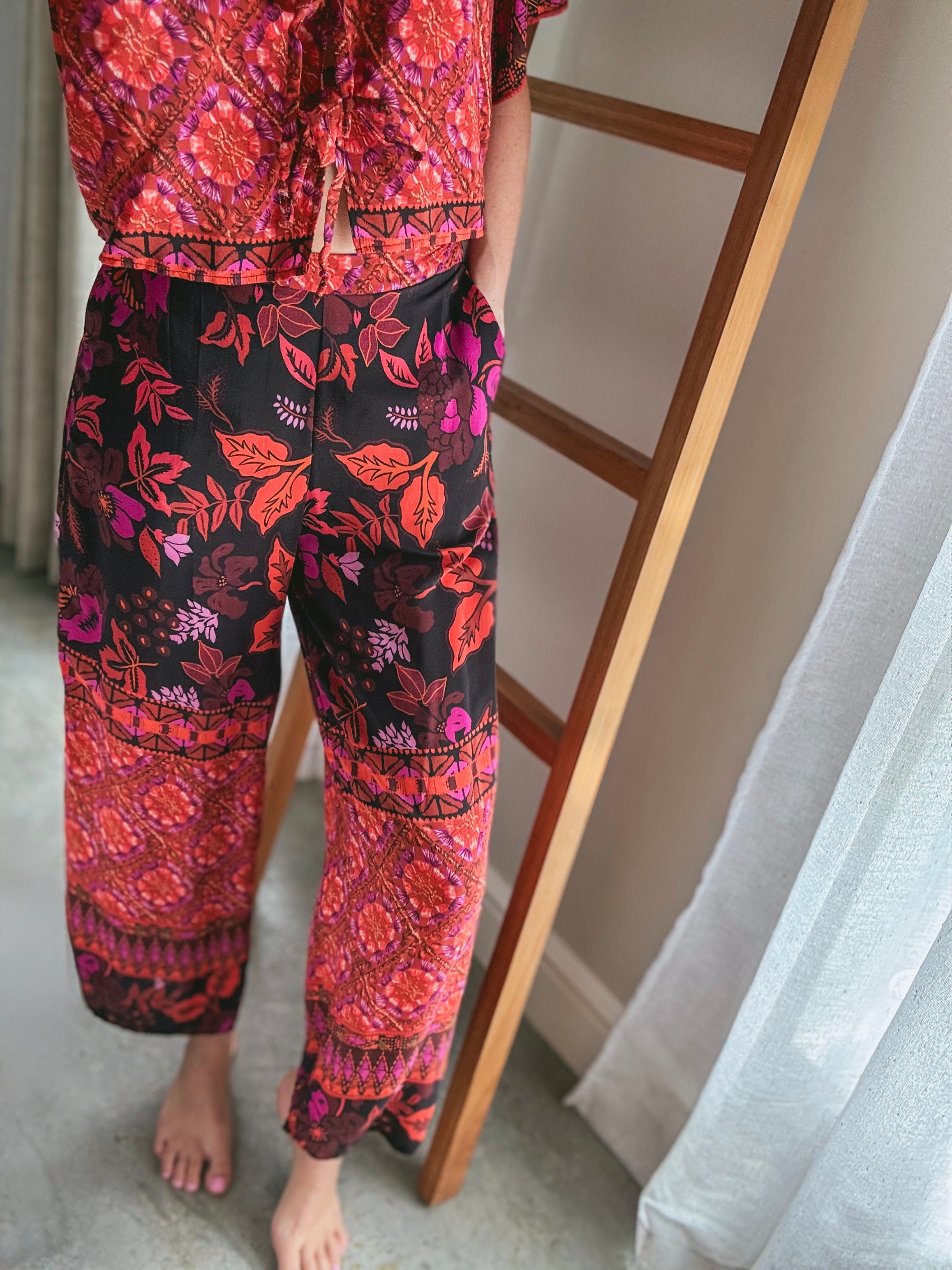 Person wearing a colourful patterned outfit standing with one hand in pants' side pocket.