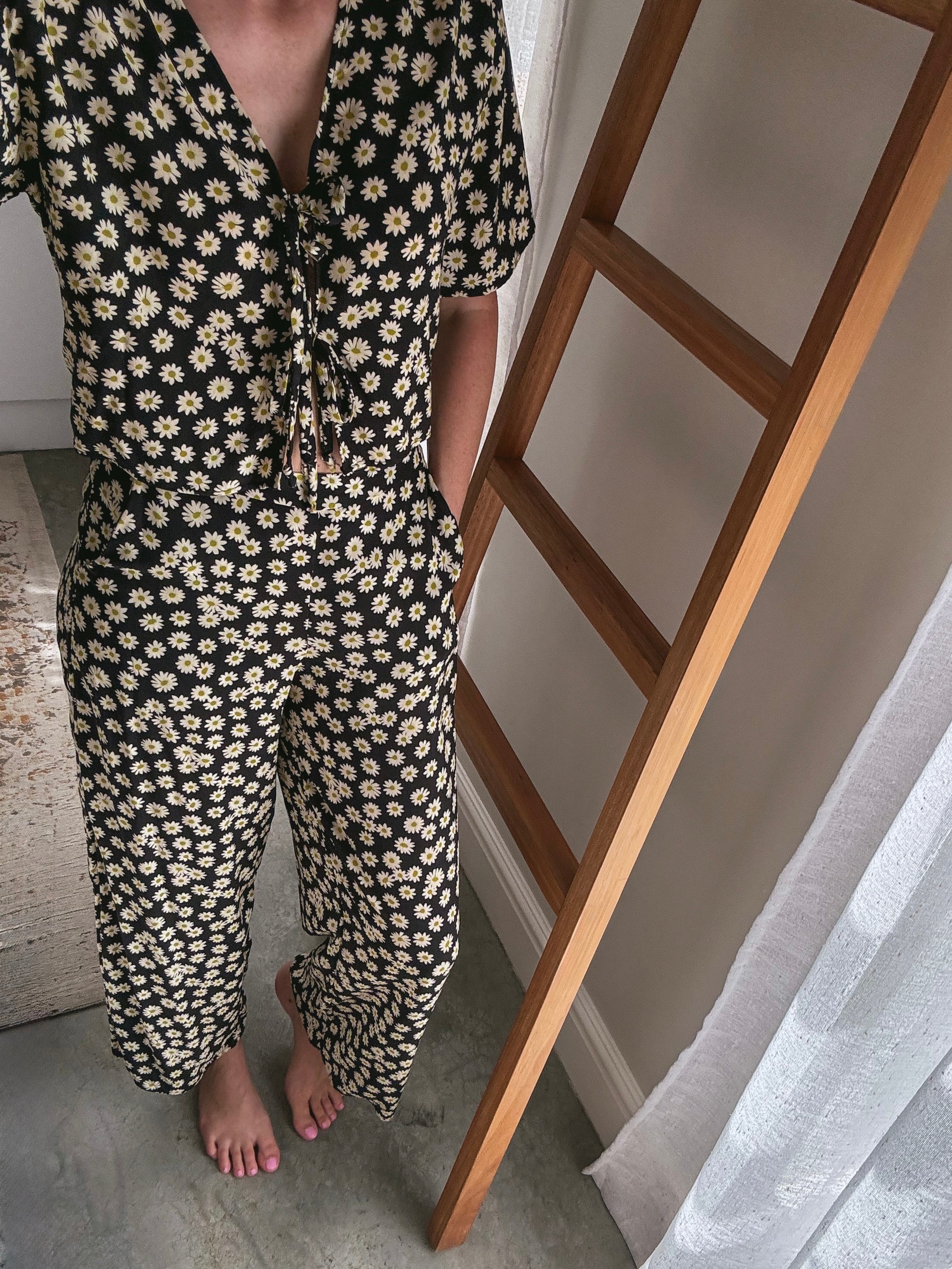 Person wearing daisy print matching set of long length pants with pockets and front tie top with short sleeves.