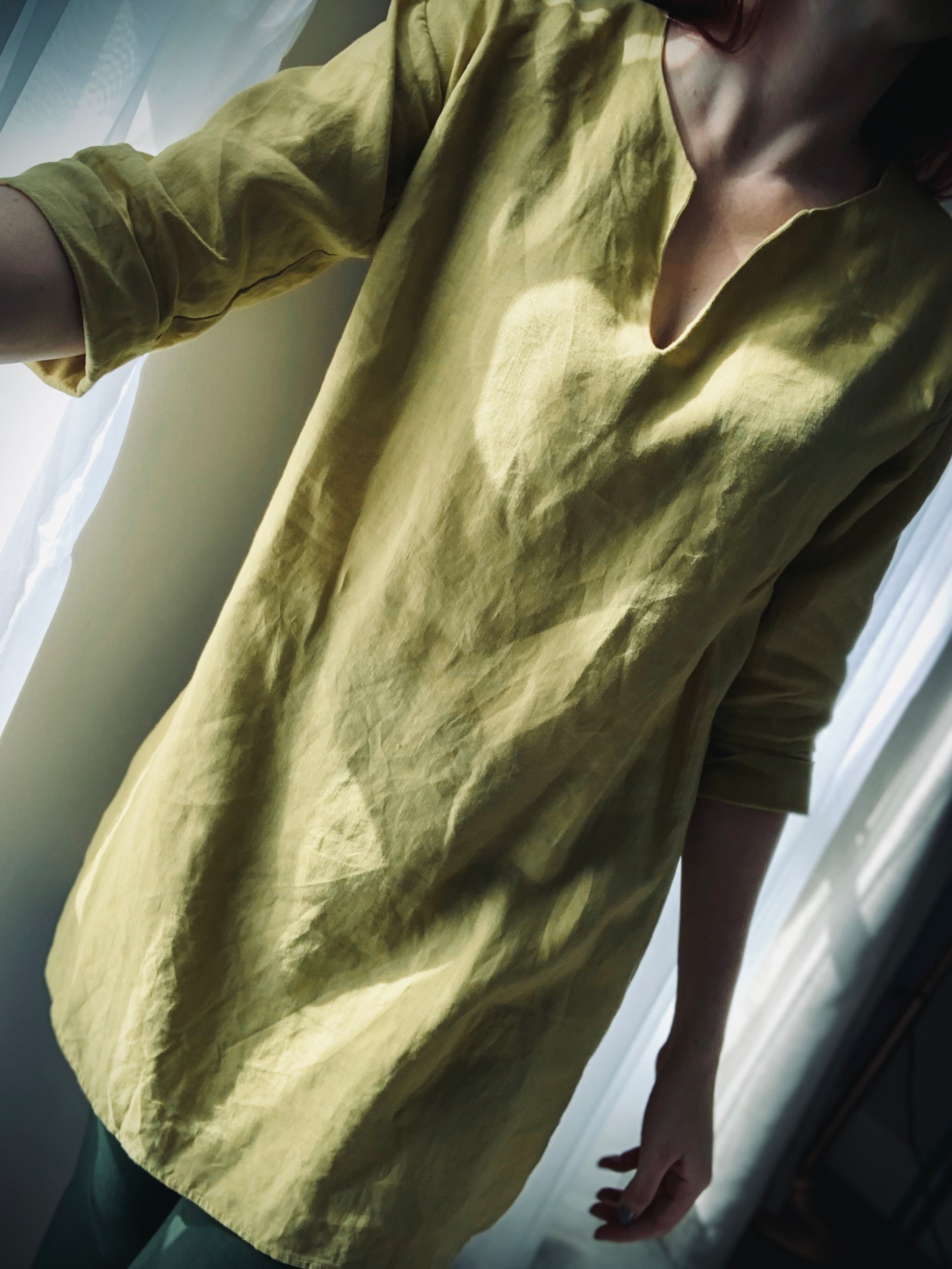 Close-up of person wearing a yellow-green linen kaftan to showcase the V-slit neckline.