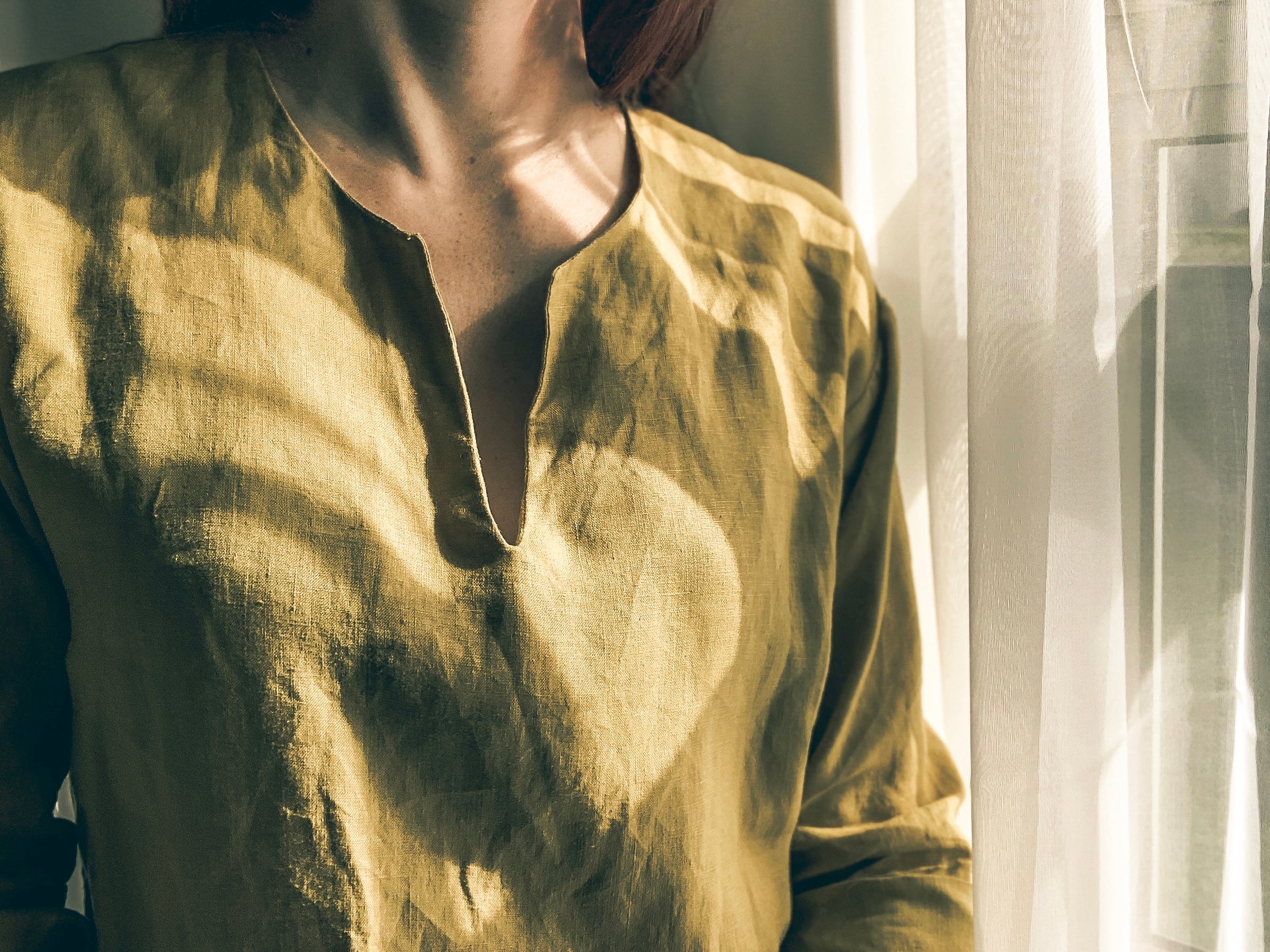 Close-up of neckline of person wearing an avocado green kaftan shirt in soft natural light.