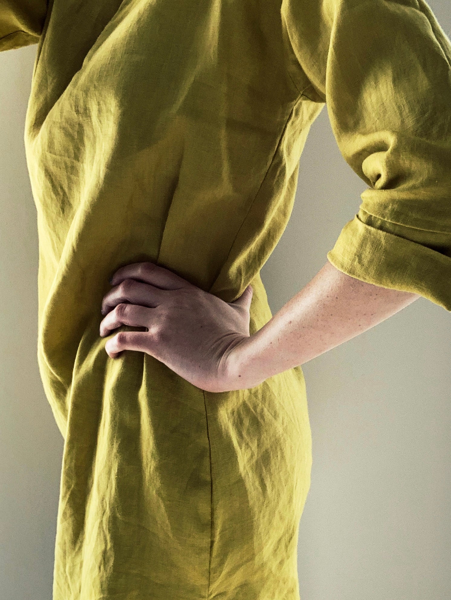 Side view of parson wearing a green pure linen dress with rolled-up sleeves against a neutral background.