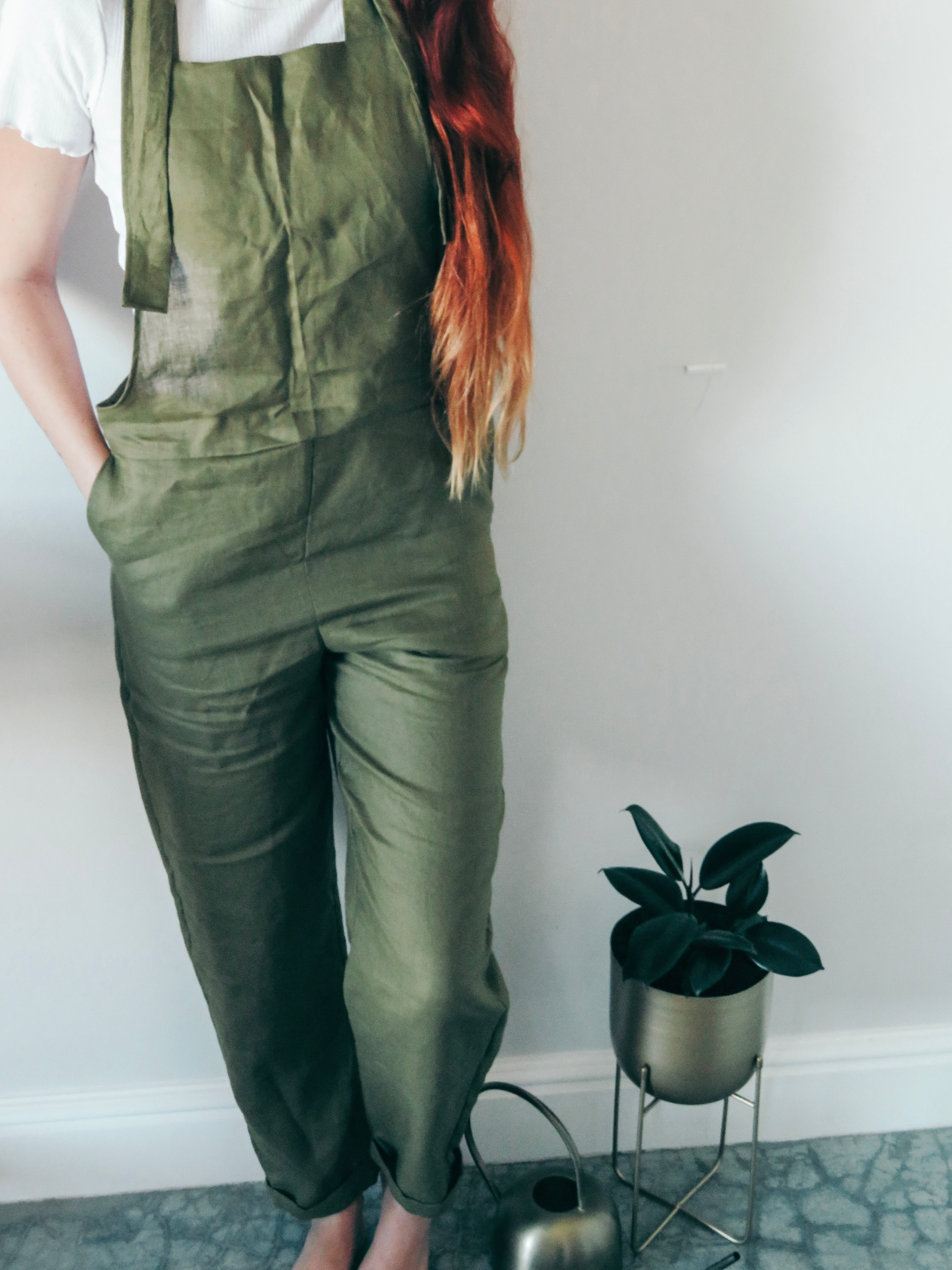 Person wearing olive green dungaree overalls with hand in side pocket.