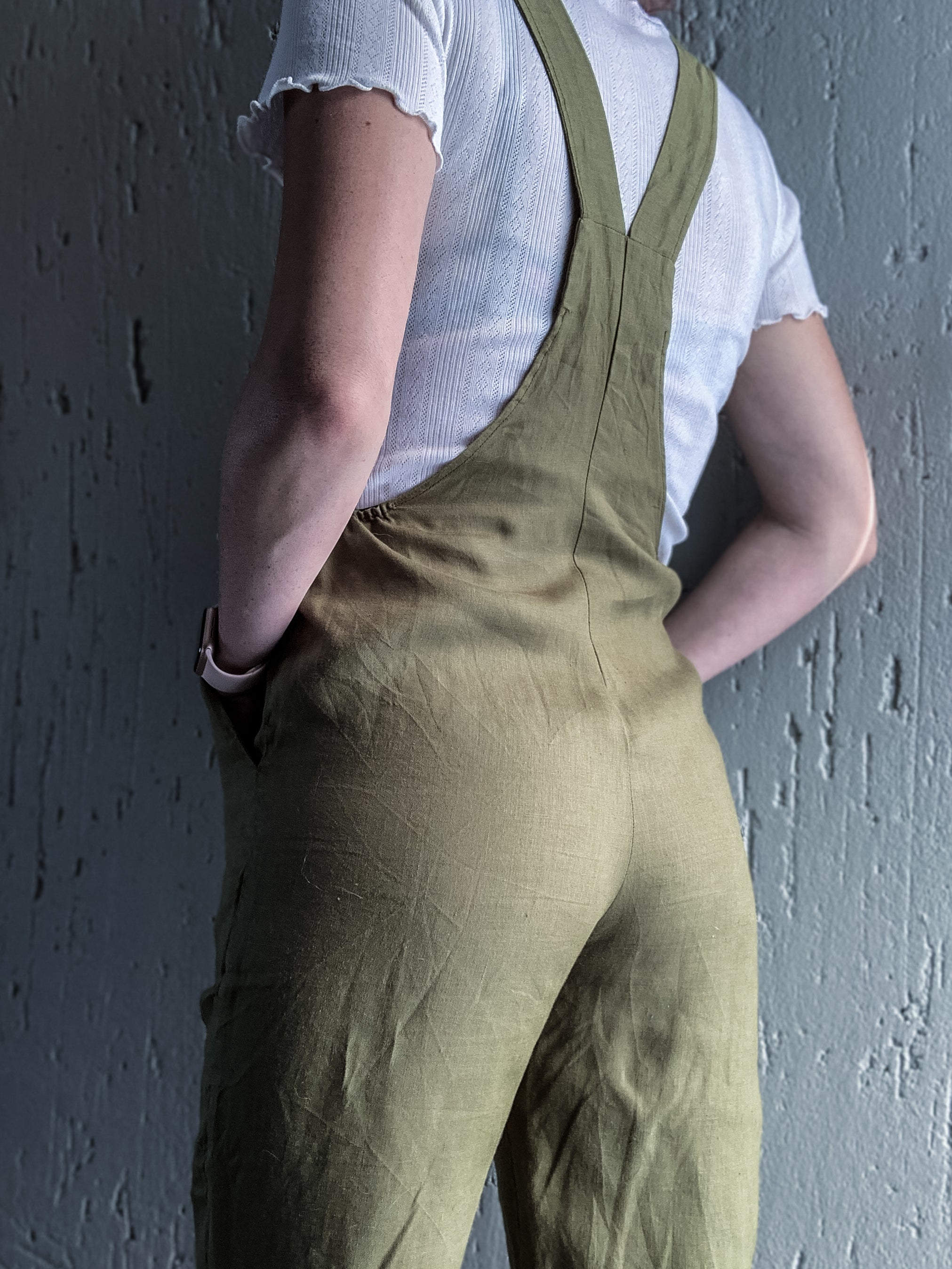 Back view of person wearing olive green dungaree overalls showcasing its practical side pockets.