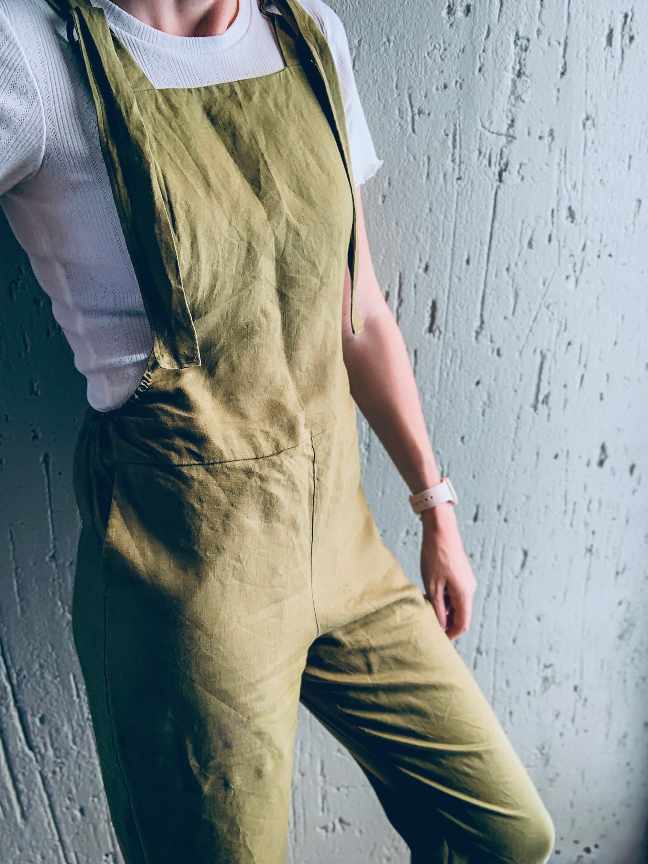 Person wearing olive green dungaree overalls showcasing its side pockets and adjustable straps.