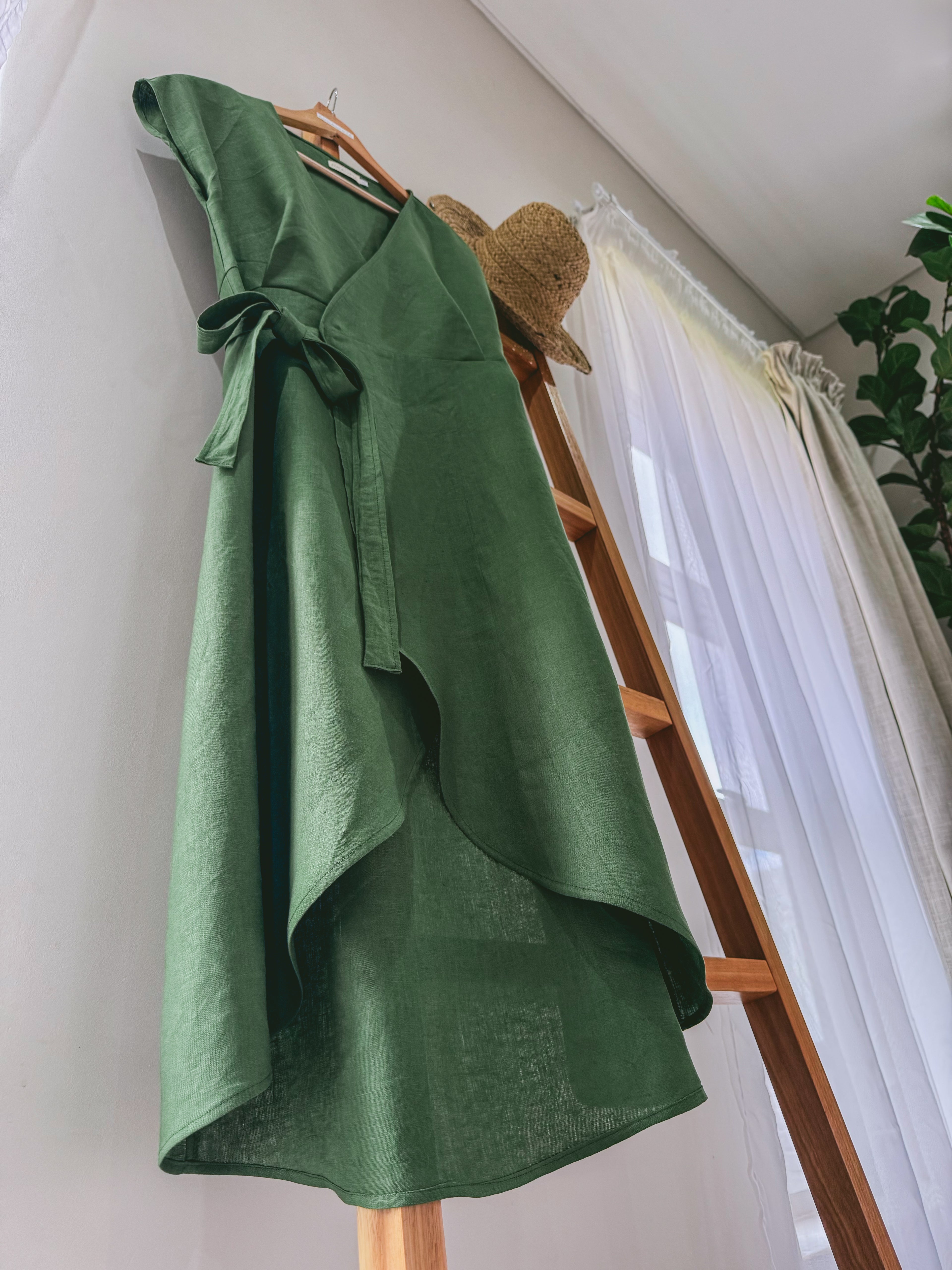 Green linen wrap dress with curved hem and side tie.