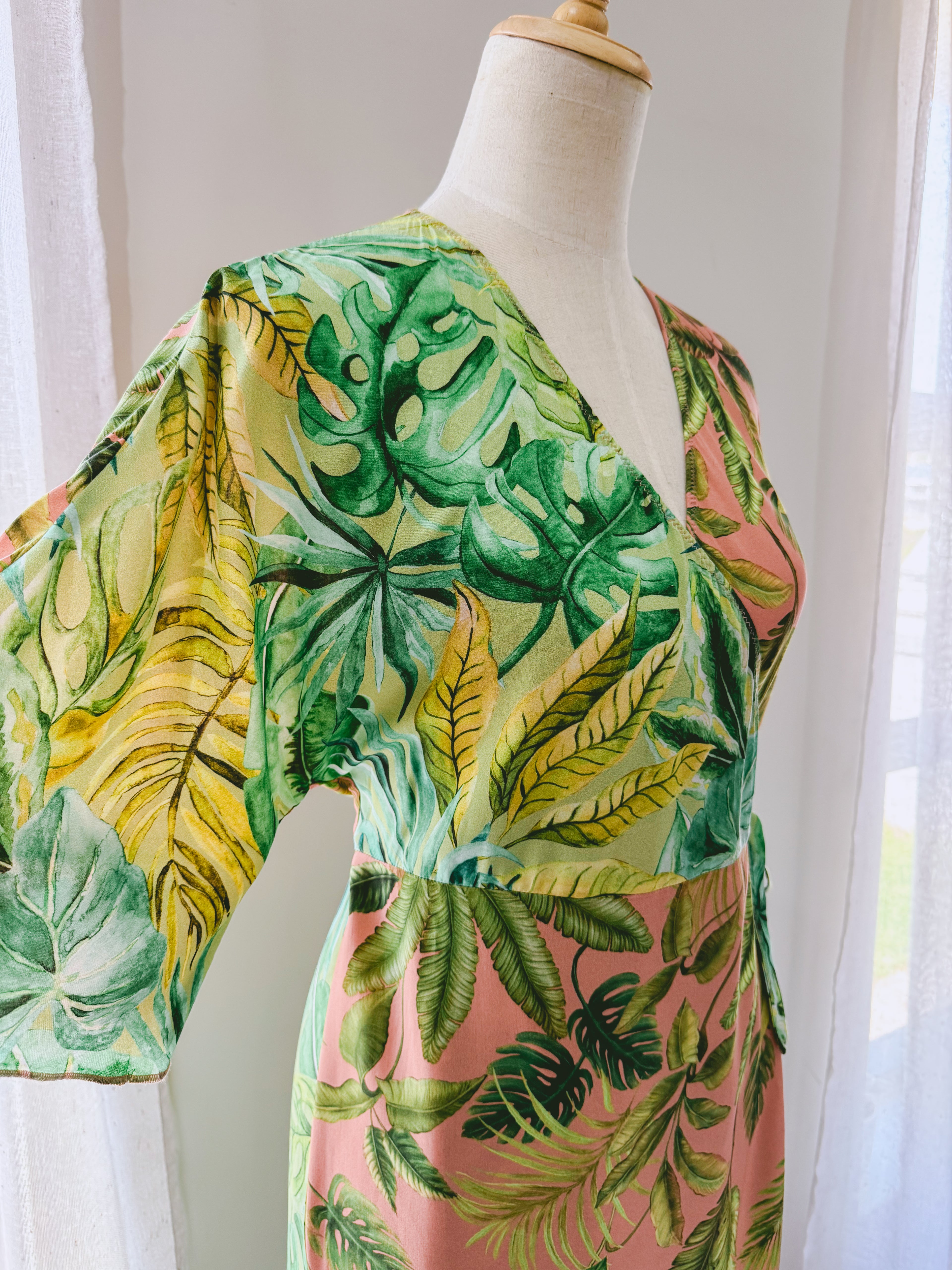 Close up of upper body of pink and green tropical leaves print wrap dress with kimono sleeves.