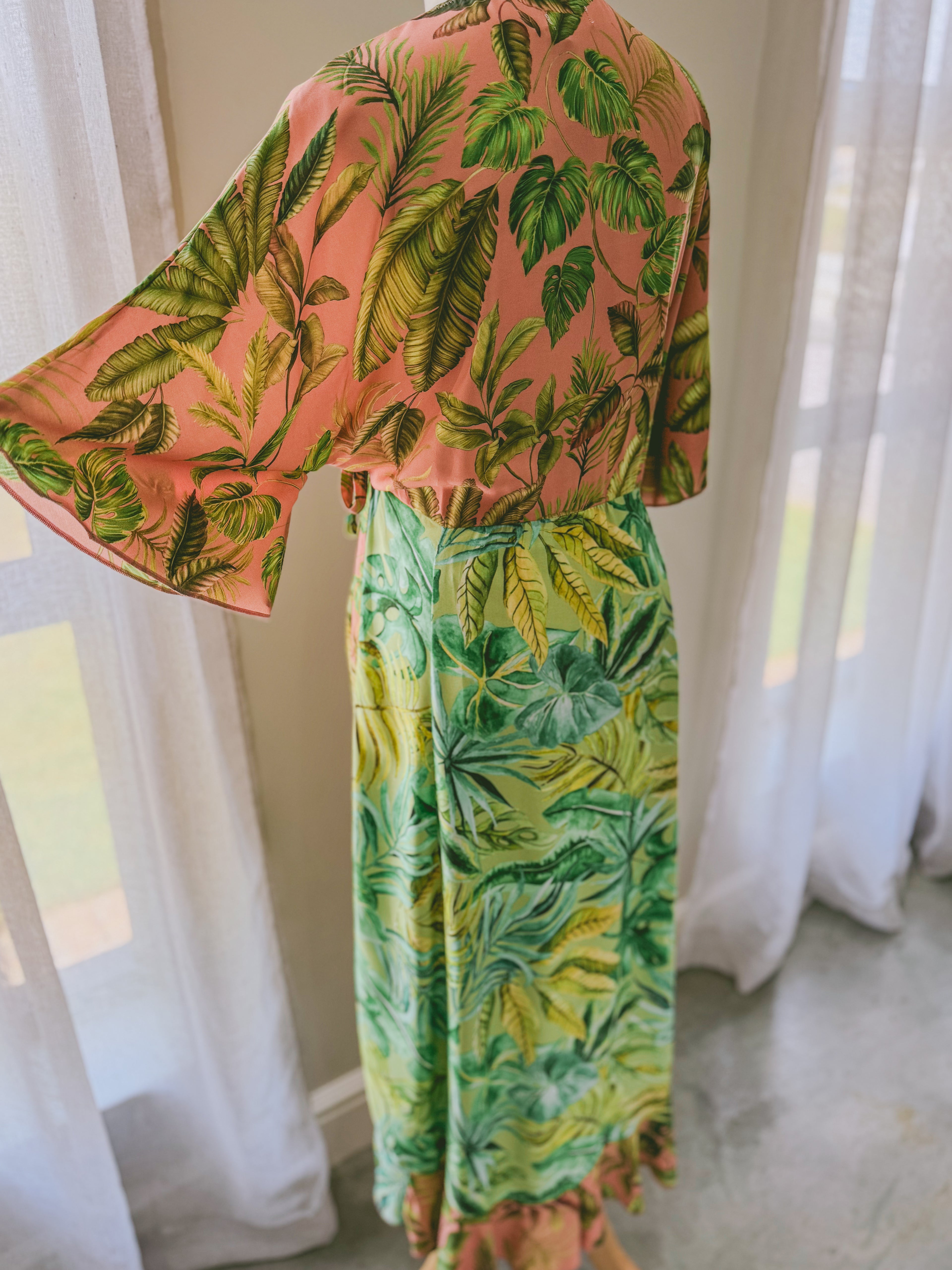 Back view of tropical patterned dress with pink top and green skirt with contrast frill.