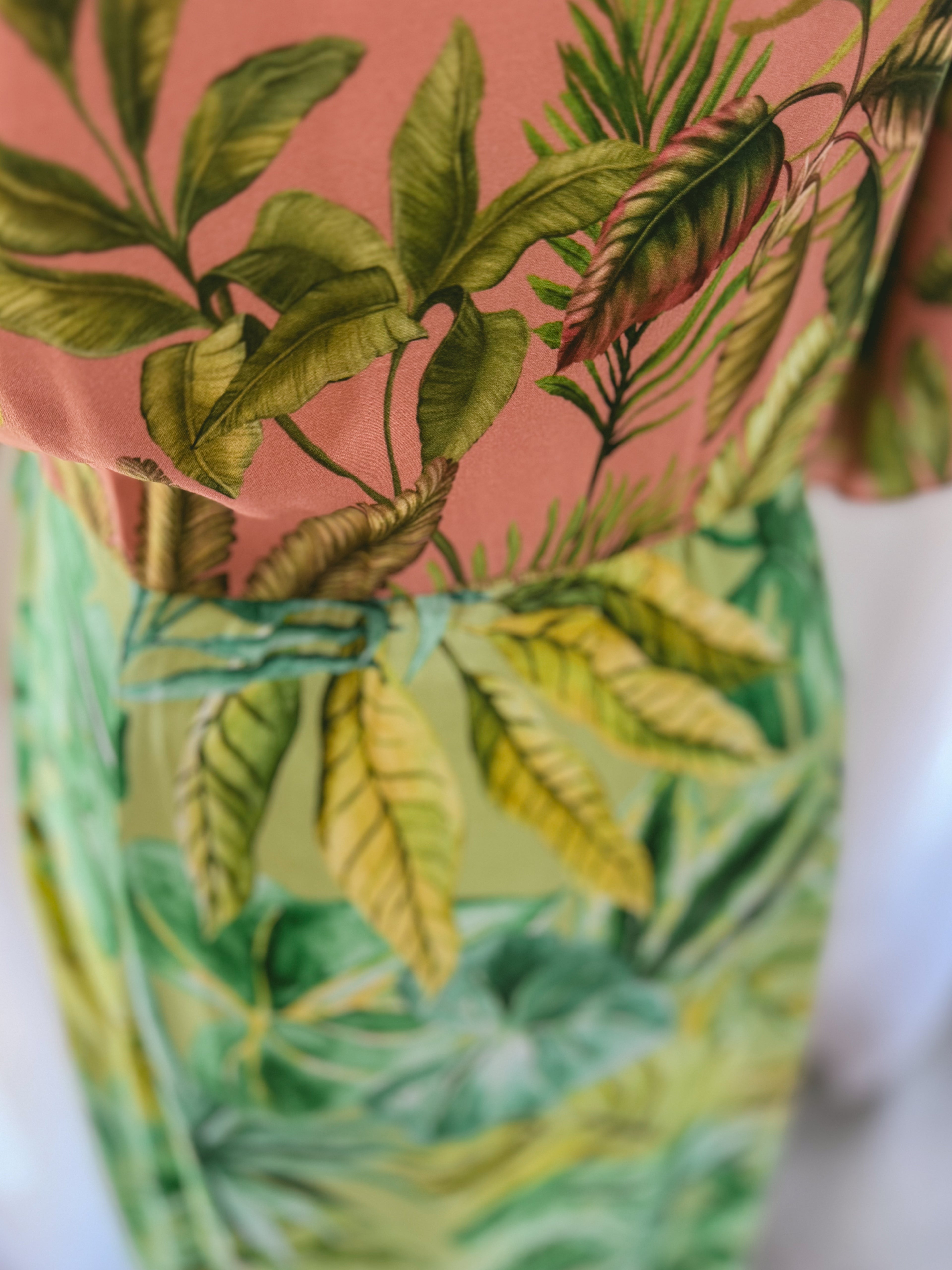 Close-up of a green leafy patterned Ecovero viscose fabric with a pink background.
