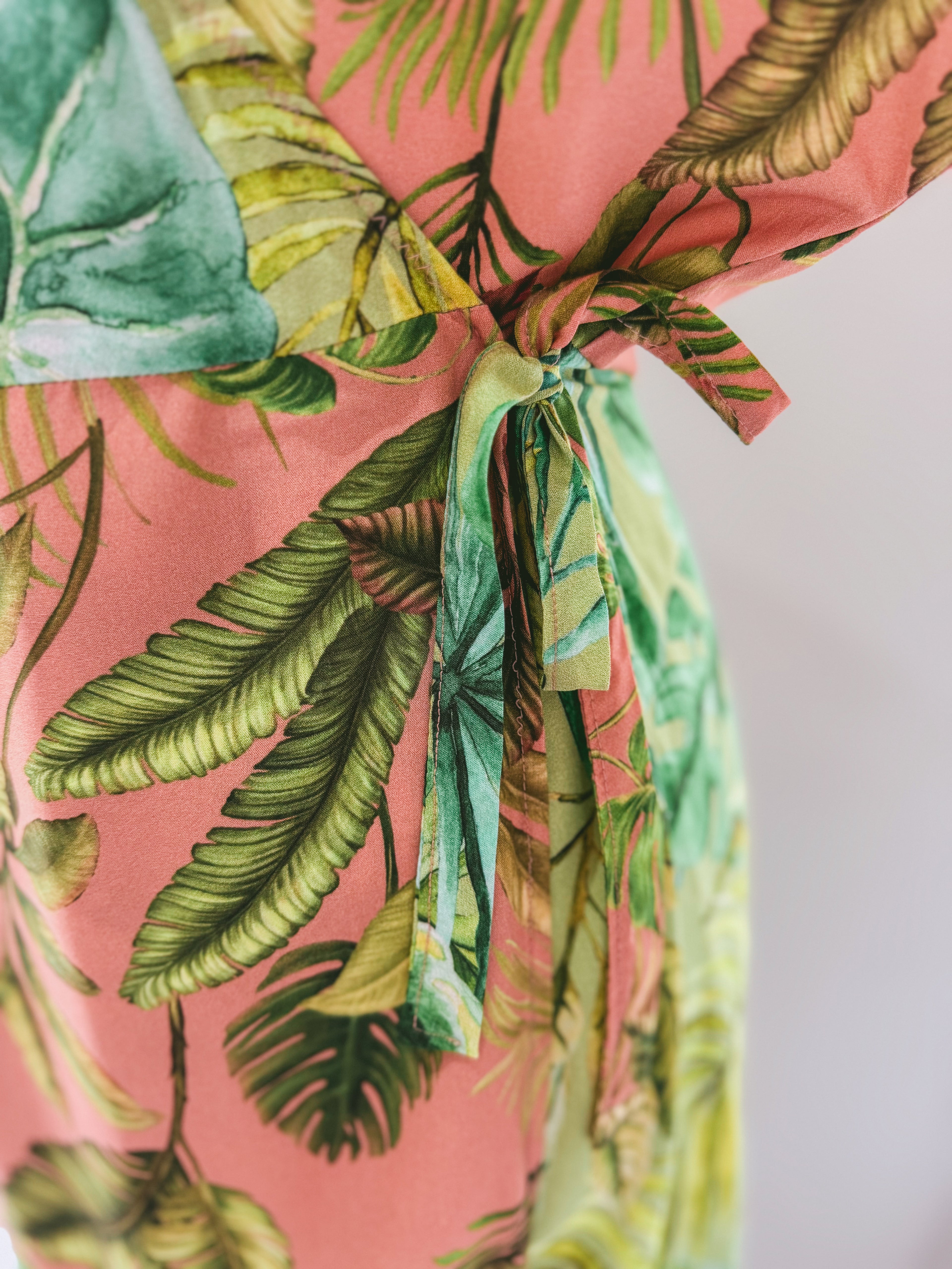 Close up of side tie detail of pink and green tropical leaves print wrap dress.
