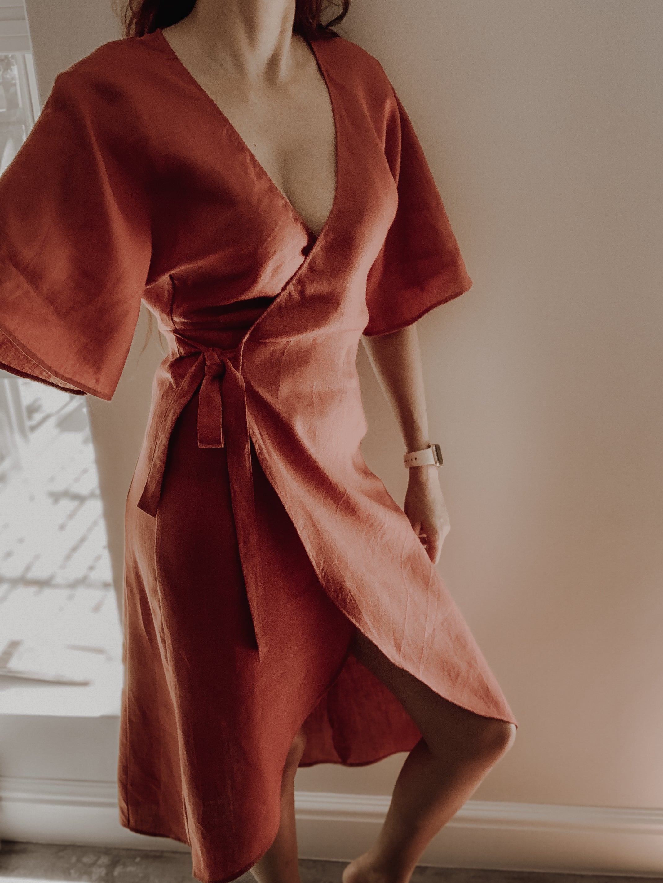 Person wearing a rust-coloured pure linen wrap dress in midi length and kimono sleeves.