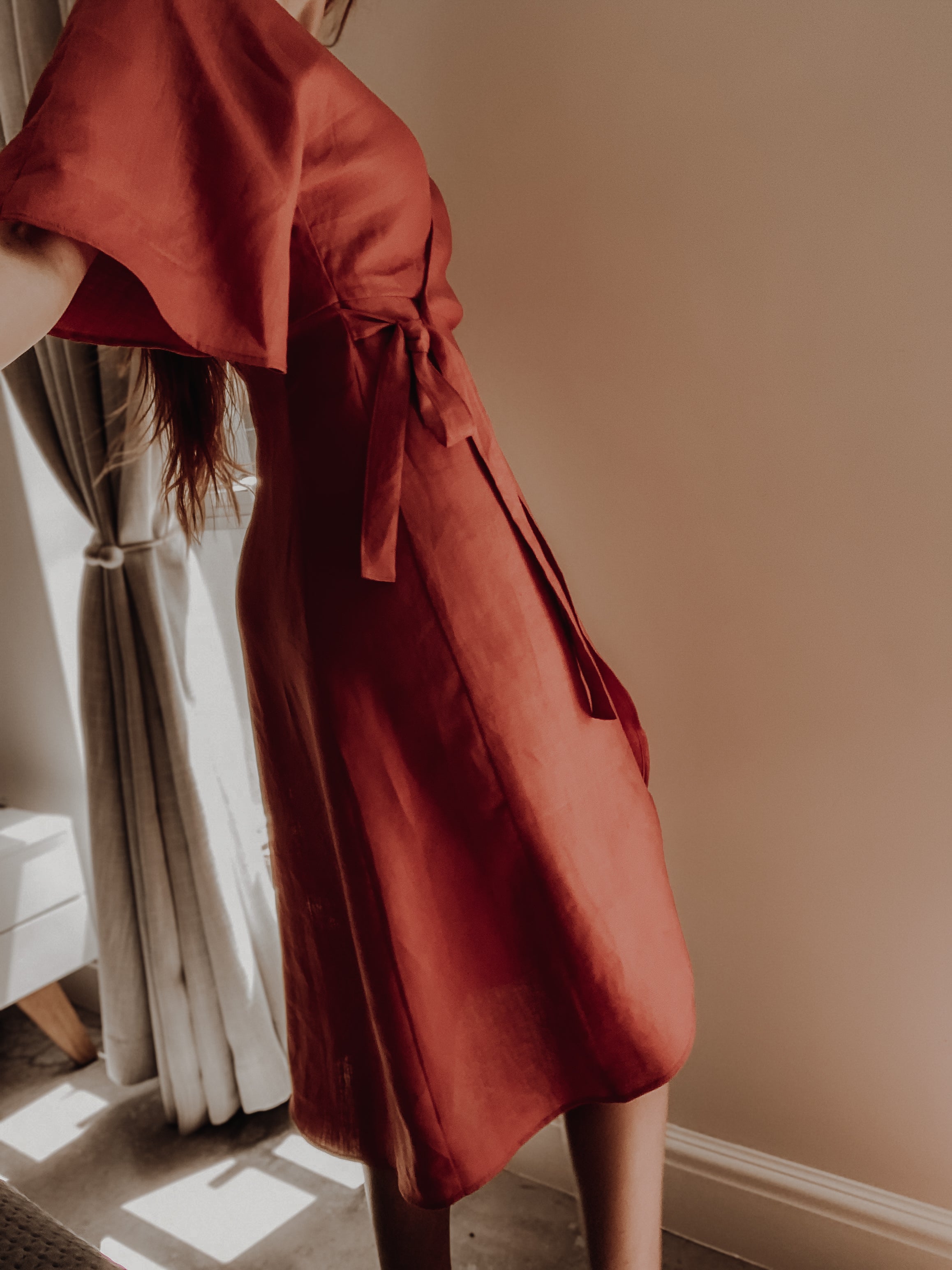 Person wearing a rust-coloured kimono sleeve wrap dress with a tie waist and sculpted side back panels.