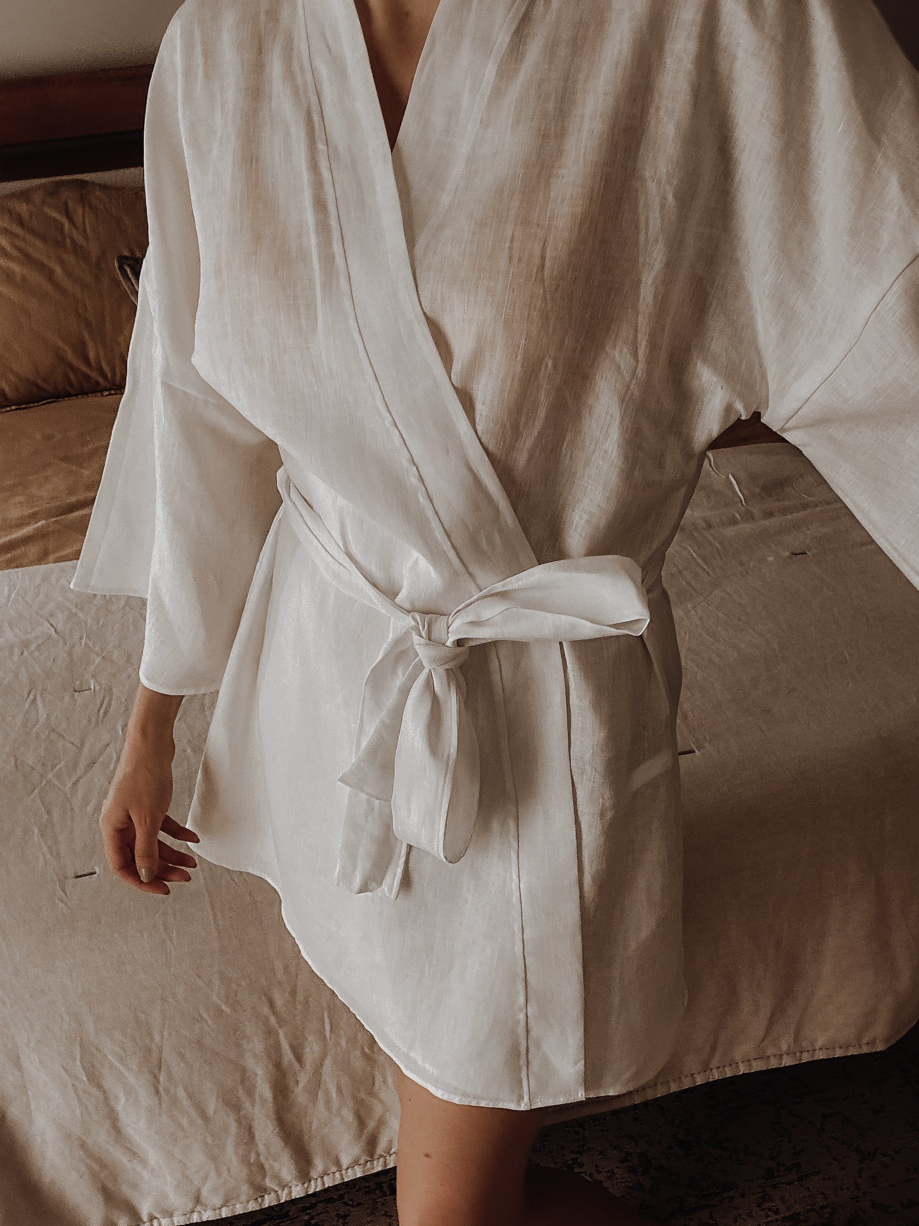 Person wearing a white pure linen robe in a bedroom setting.