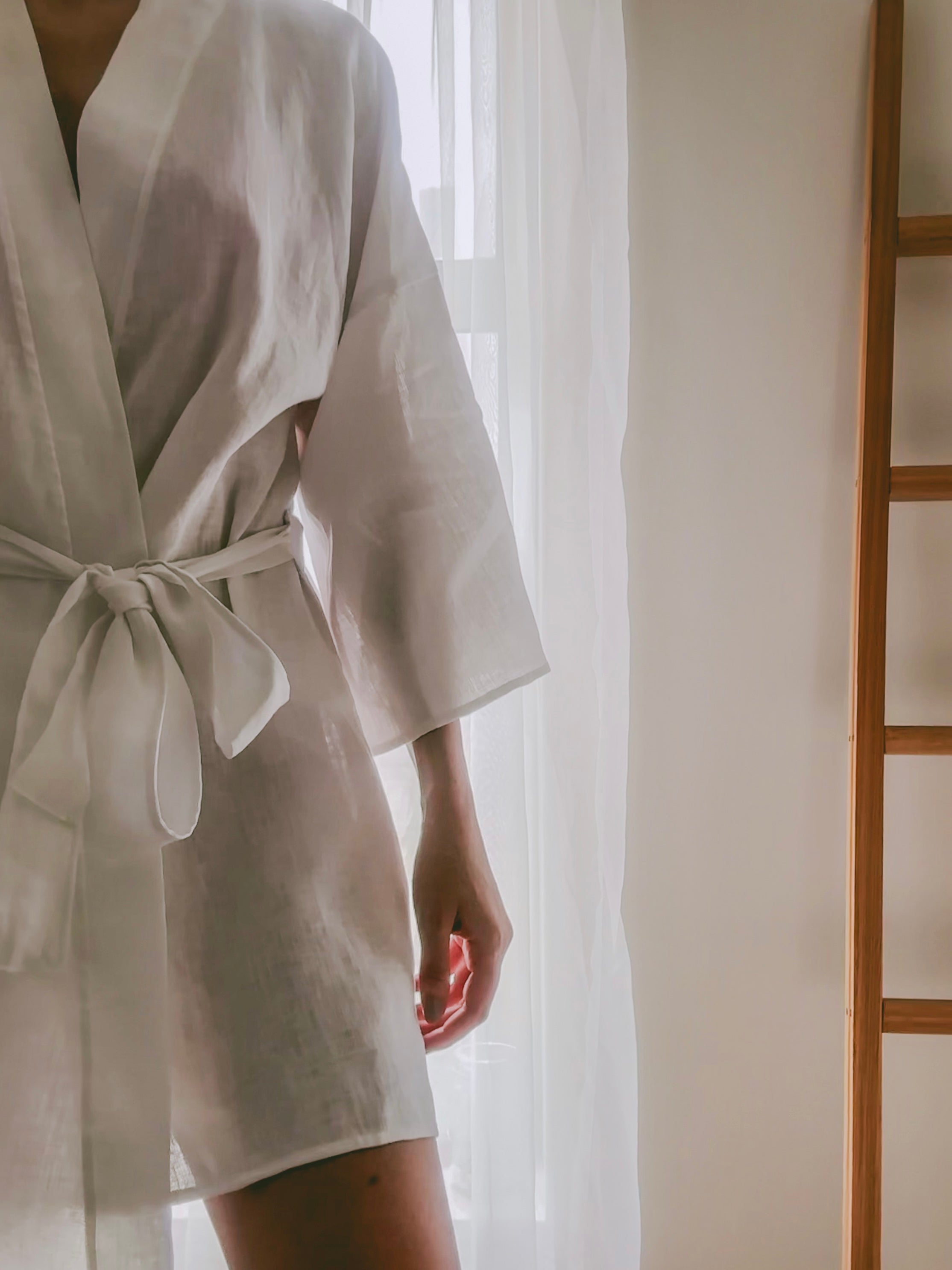 Bride wearing a white pure linen mini length robe in a softly lit room the morning of her wedding getting ready.