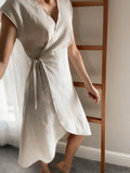 Women wearing a natural colour linen wrap dress with cap sleeve and curved hem.