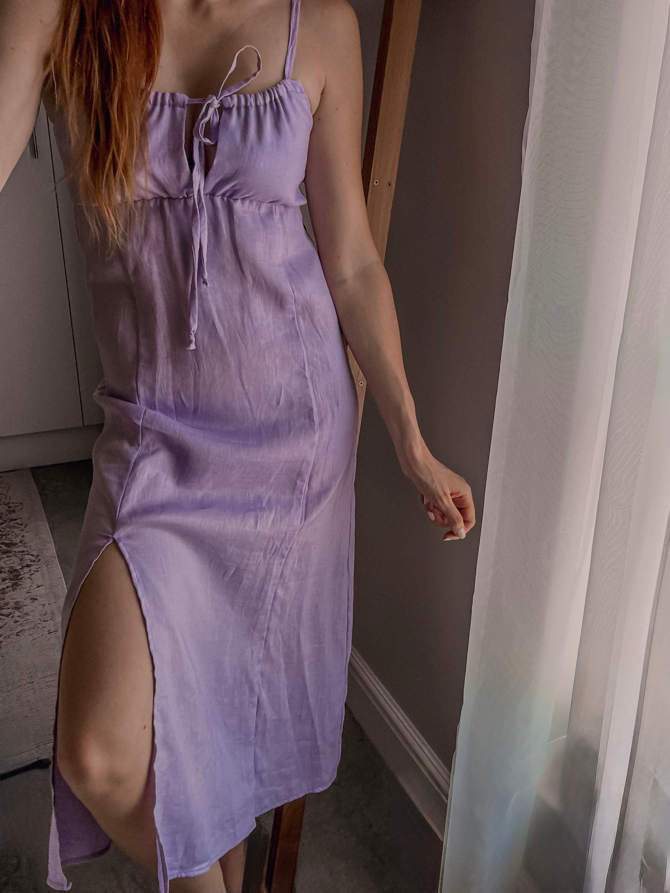 Person wearing a lilac colour milkmaid style dress with adjustable ruching detail at the front top, adjustable straps and front knee slit at midi length.
