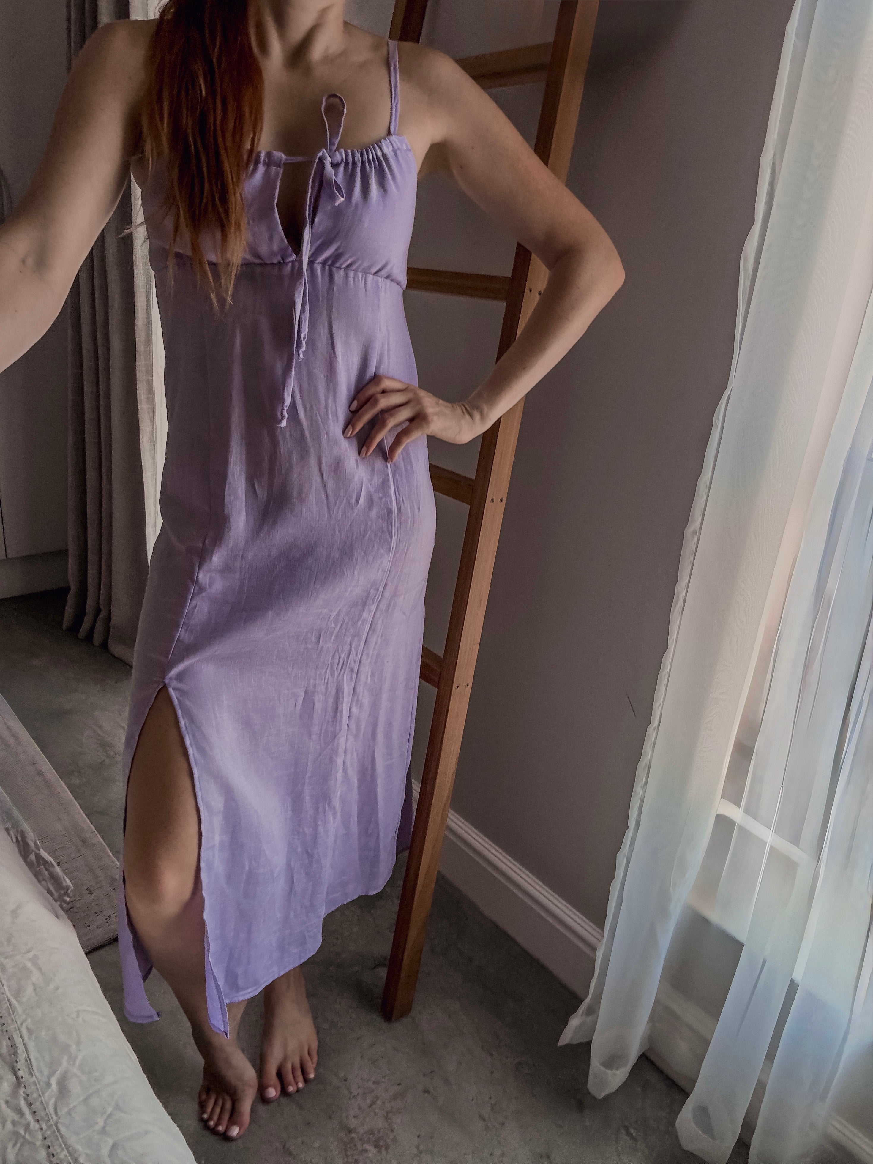 Person wearing a lilac colour milkmaid style dress with adjustable ruching detail at the bust area and front knee slit for ease of movement.