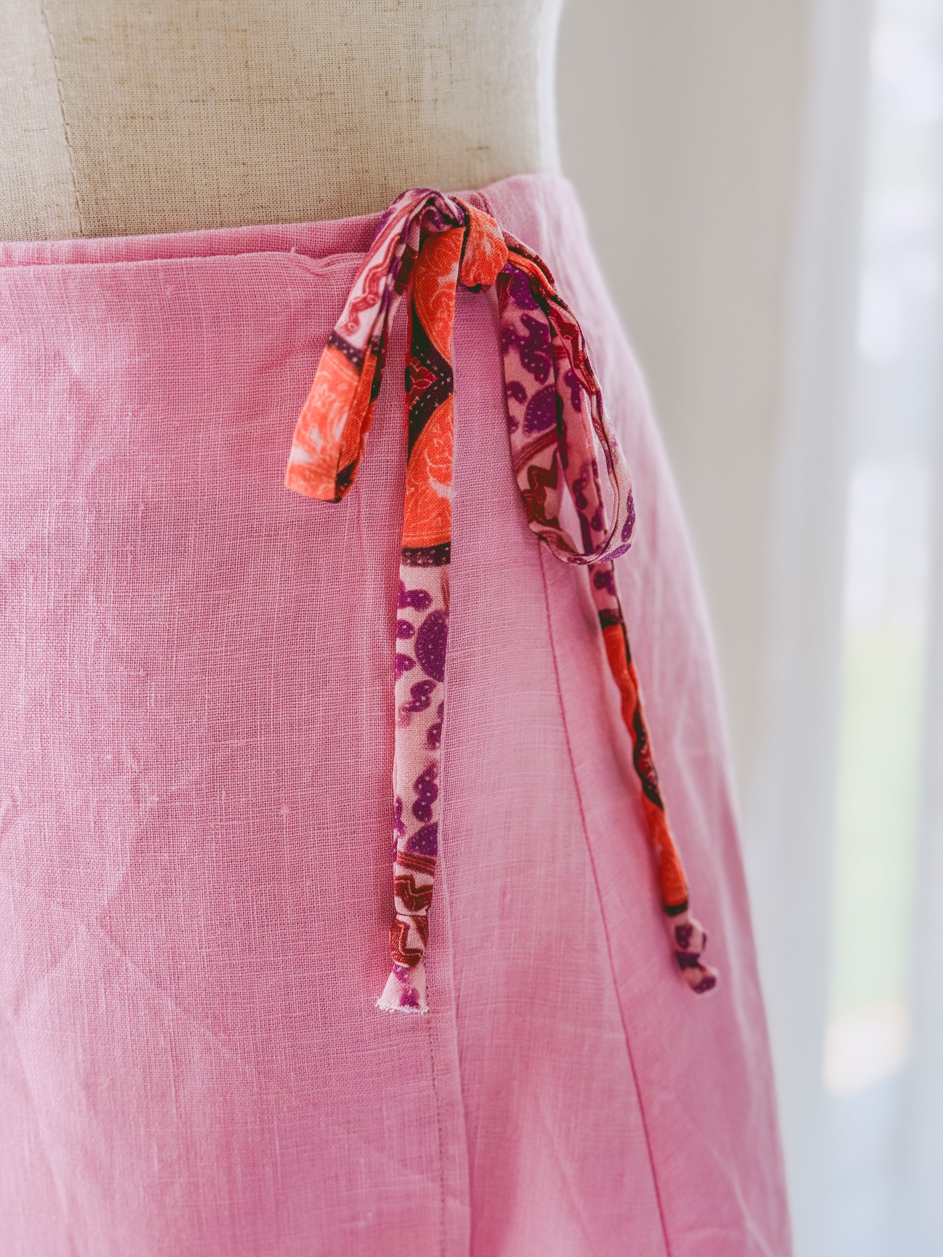 Close-up of a pink linen skirt with colourful Ecovero Viscose side ties on a mannequin.
