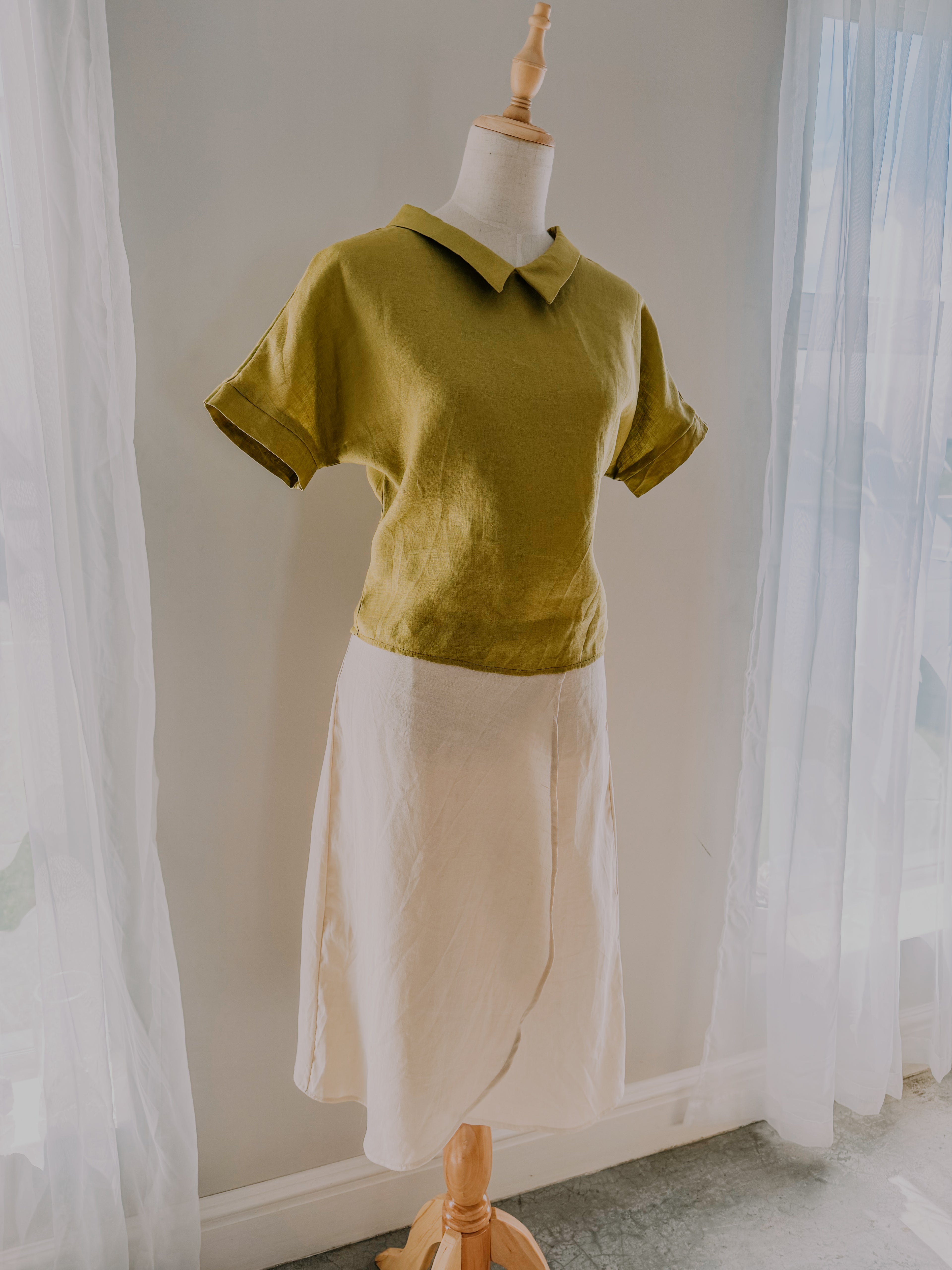 Mannequin wearing a green pure linen shirt paired with light beige skirt.