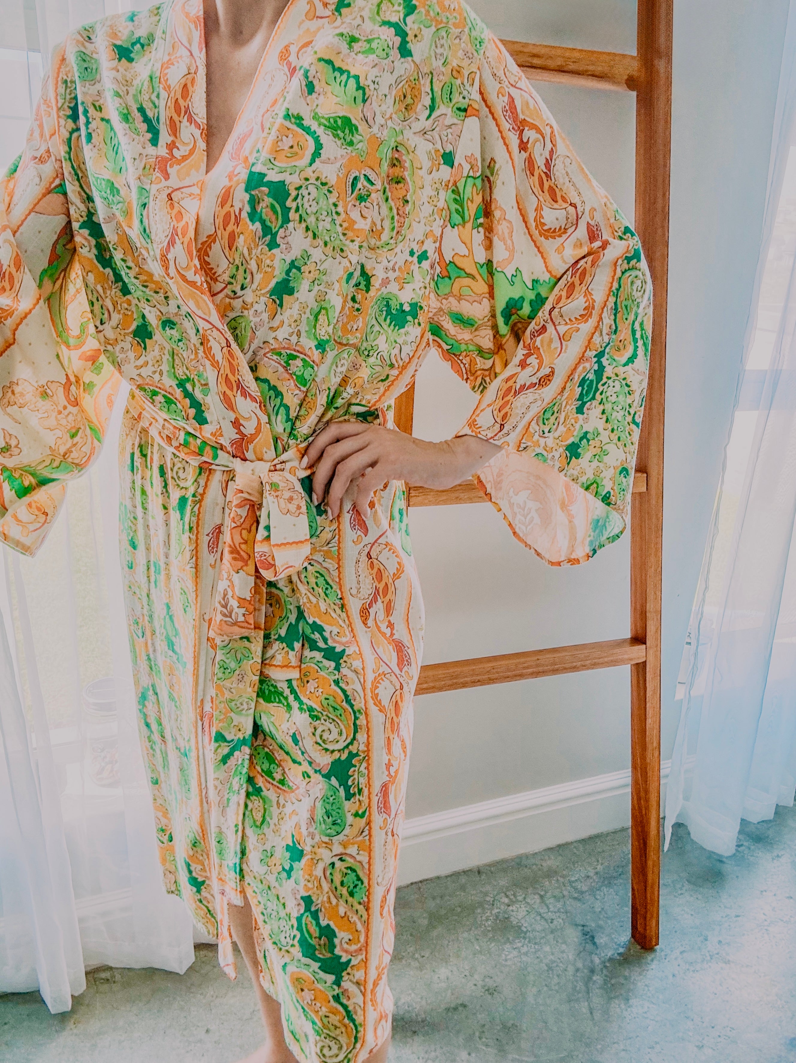 Person wearing a paisley print kimono gown in green and orange tones made from ecovero viscose linen.