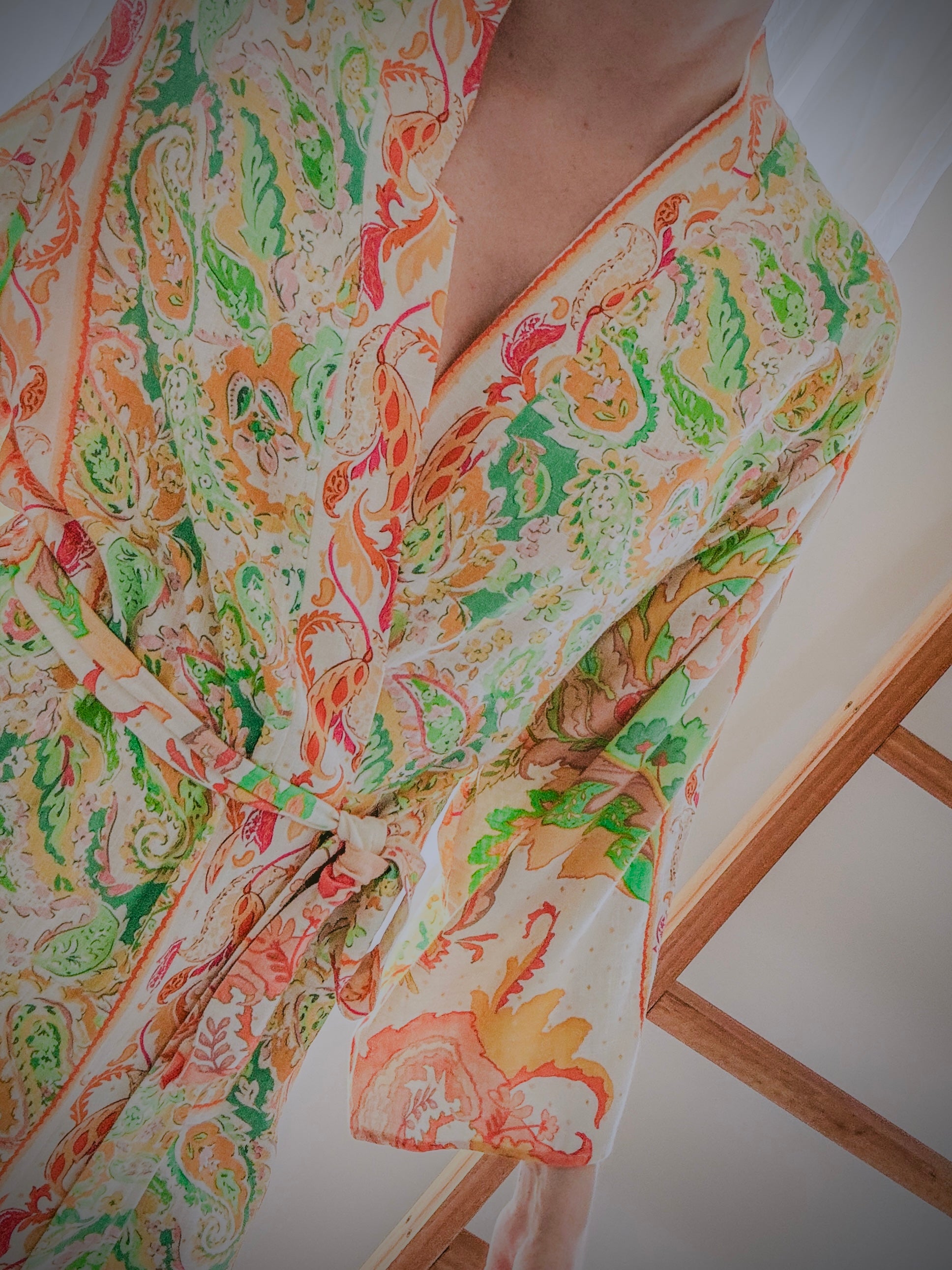 Close up of the front view of parson wearing a colourful paisley patterned kimono gown made from ecovero viscose linen.