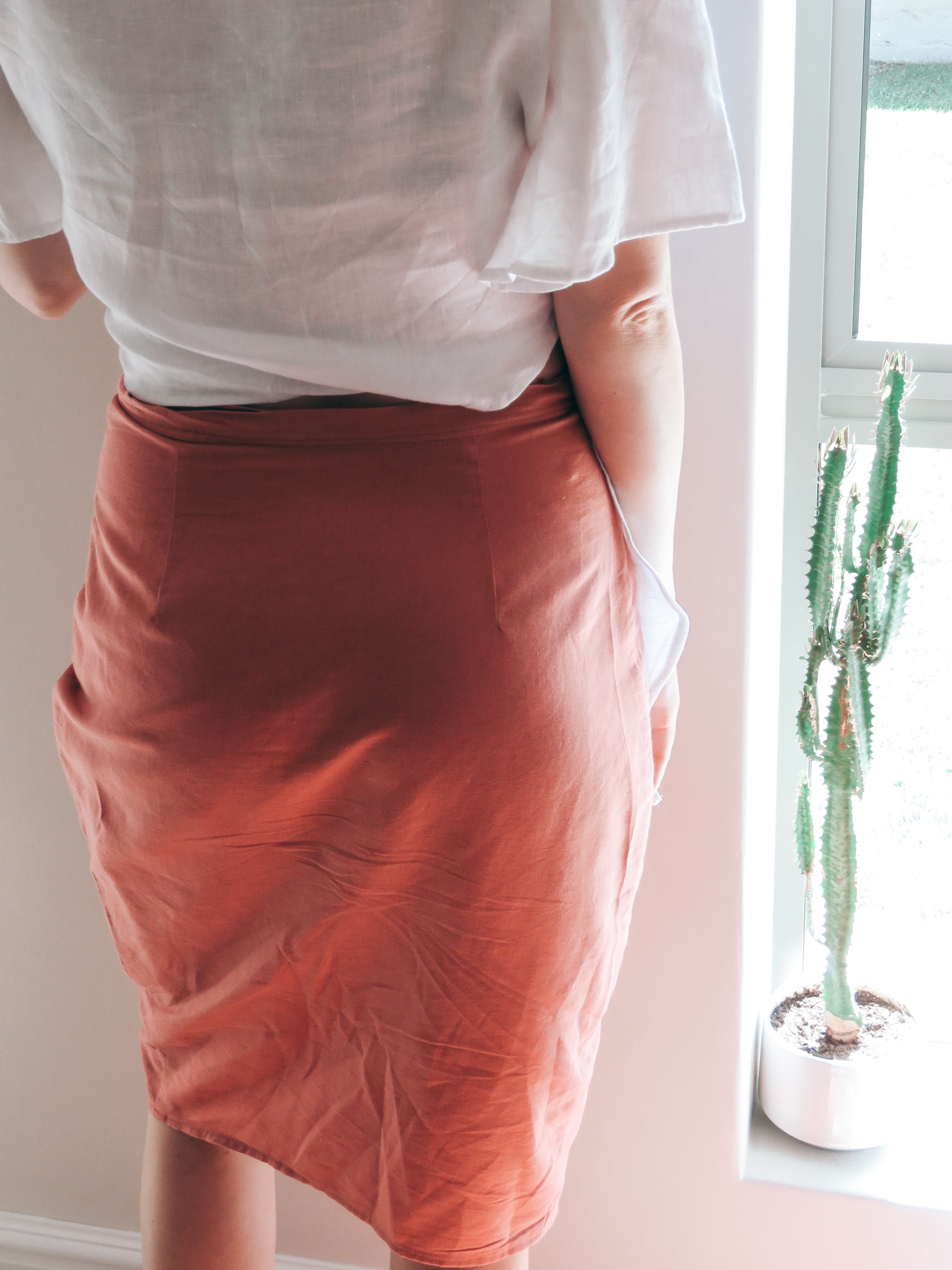 Back view of person wearing a coral colour pure linen fitted wrap skirt with back darts.