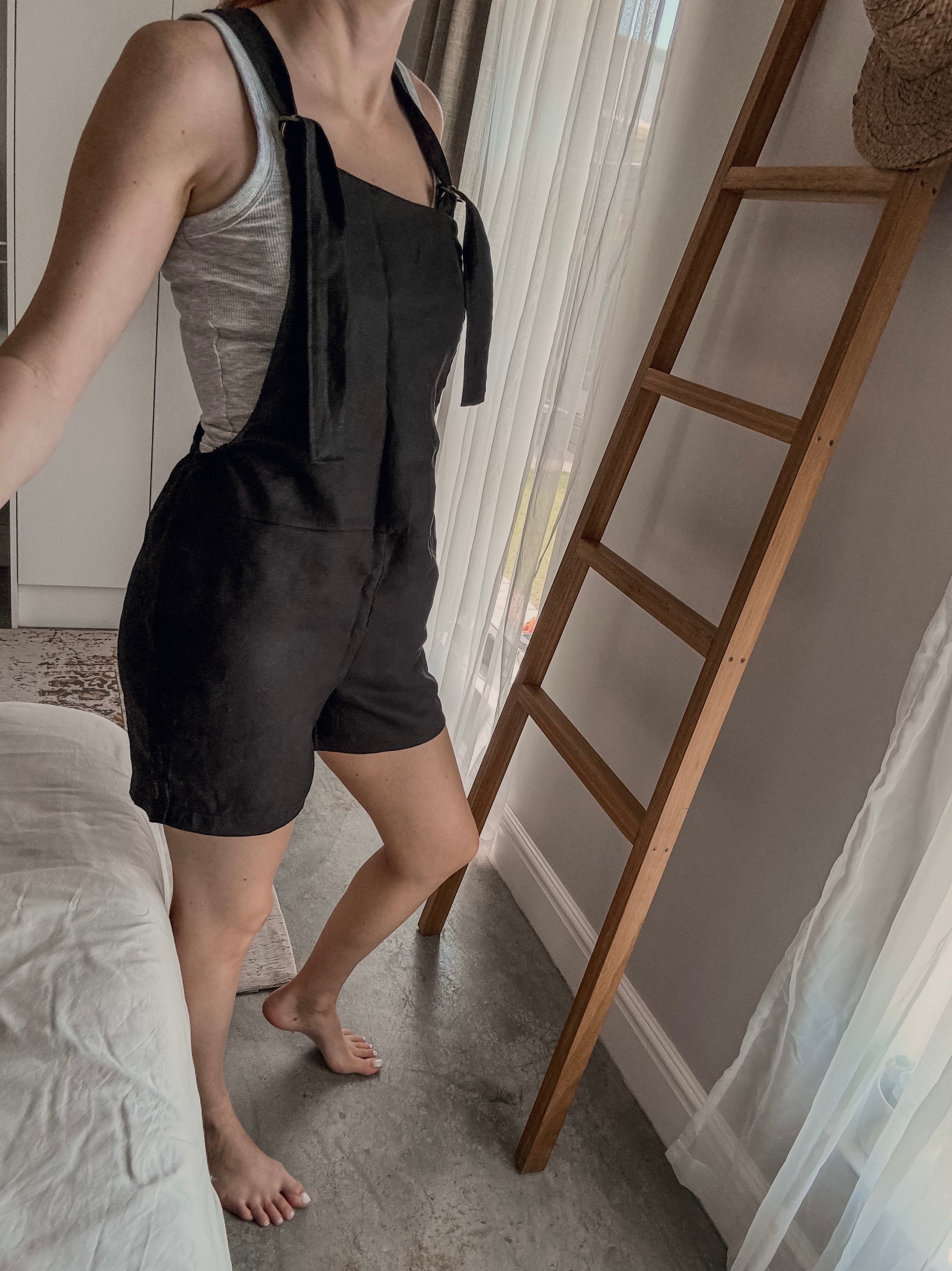 Person wearing an black short overall romper made from black linen and adjustable straps.